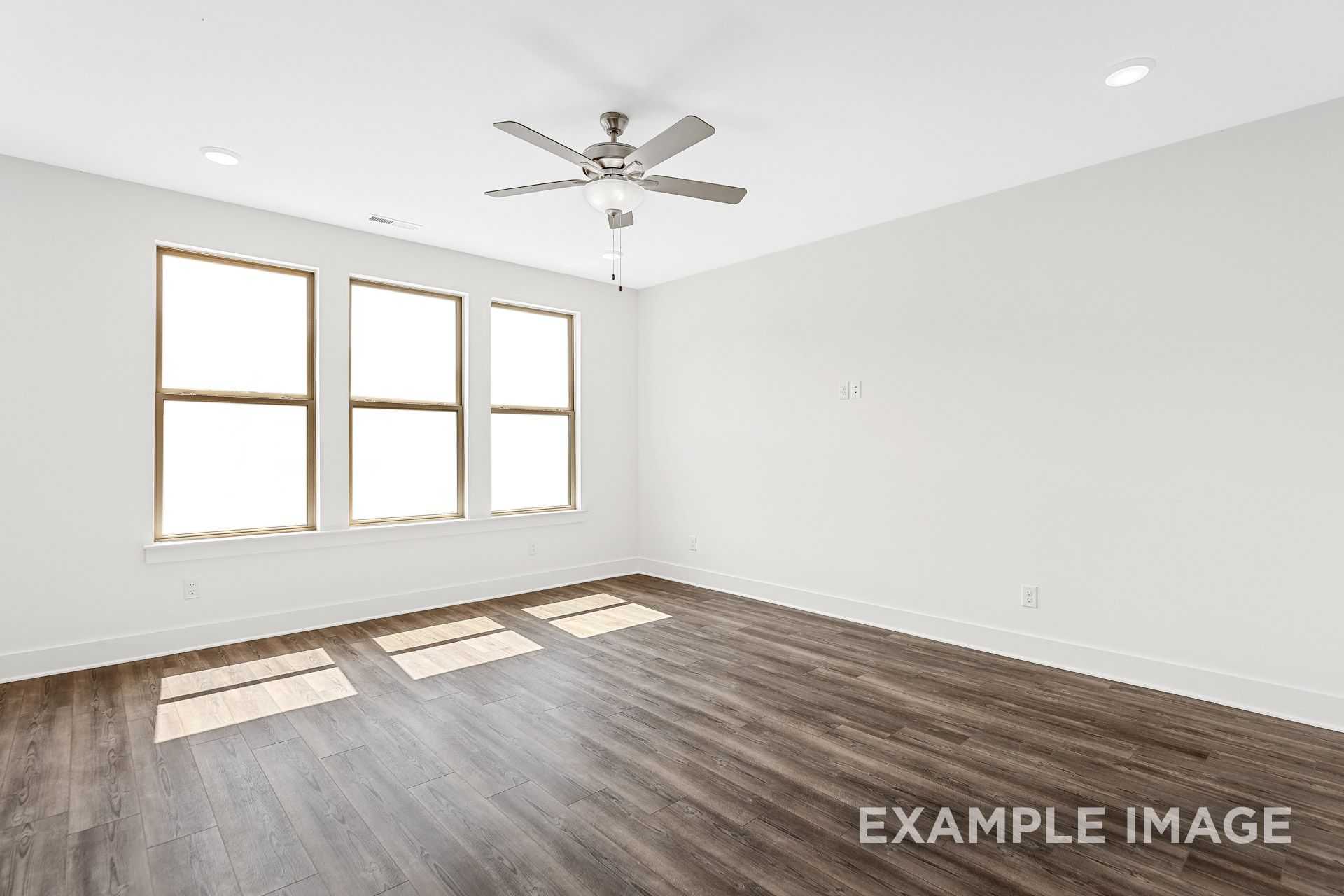 Spacious master bedroom in The Logan B with large triple windows, ceiling fan, hardwood floors, and natural light
