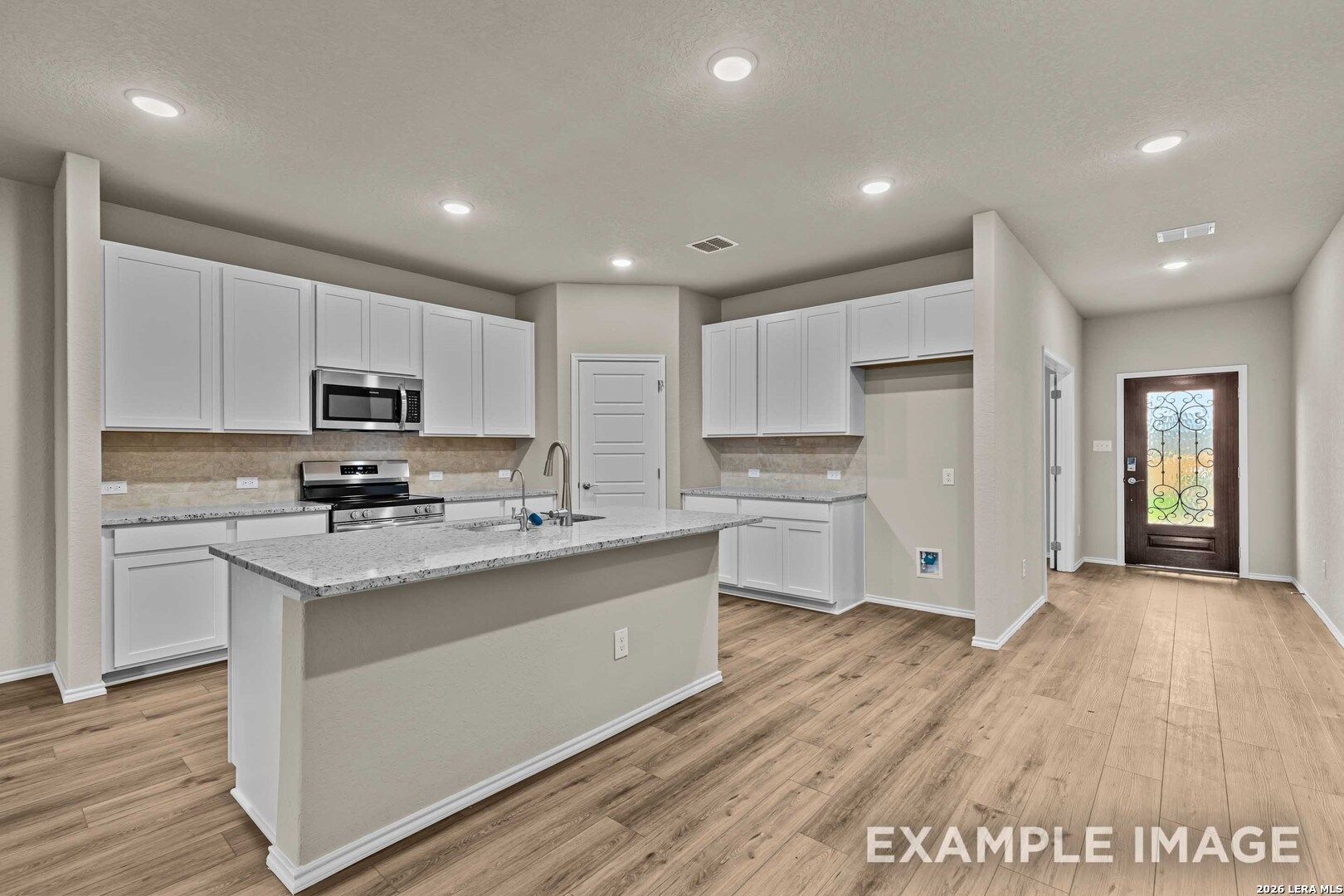Modern kitchen with white cabinets, granite island, and wood-style flooring in The Douglas F floor plan, Bricewood, TX.