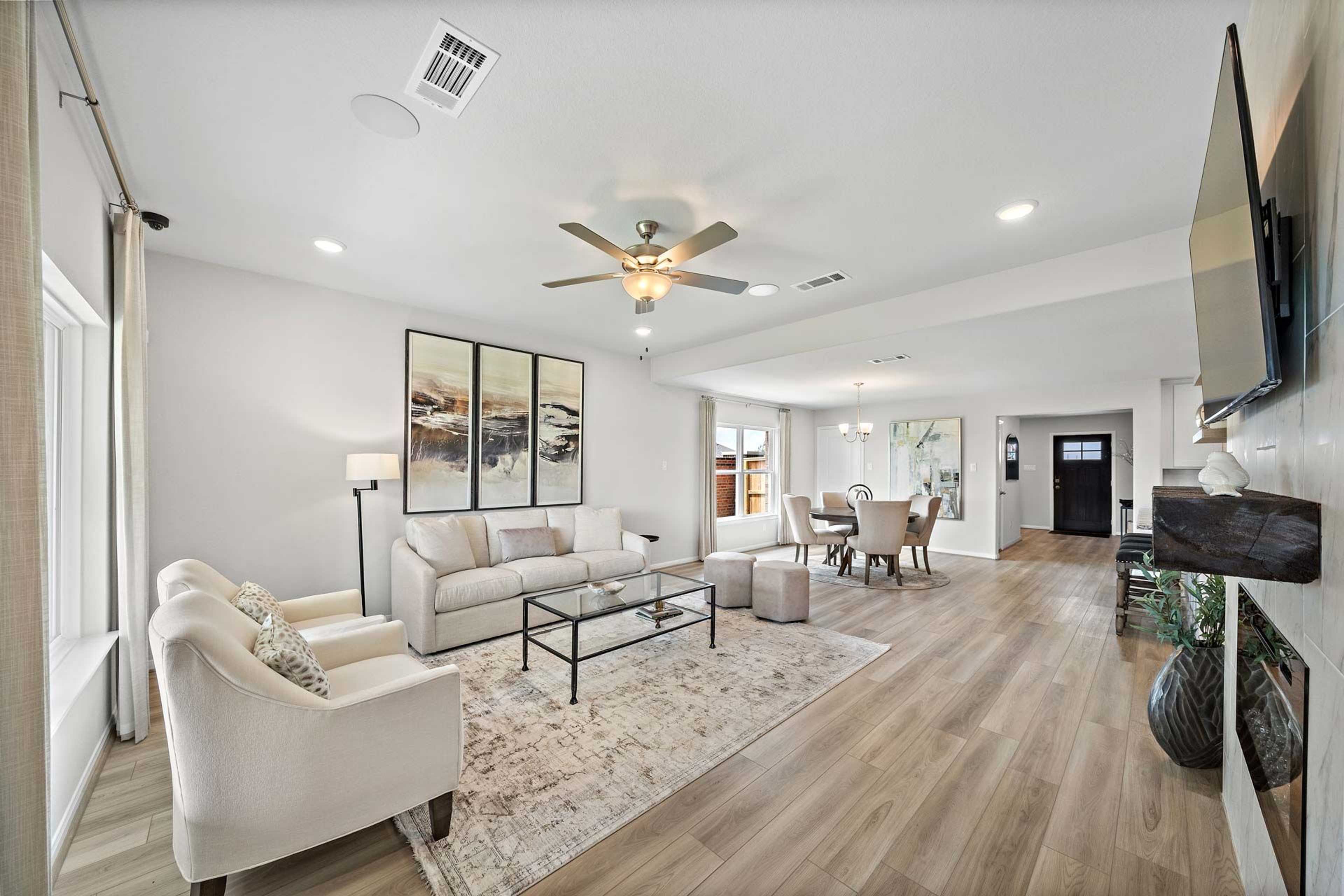 Open-concept living room at Enclave at Newport in Crosby Texas with beige sofa, ceiling fan, hardwood floors and dining area