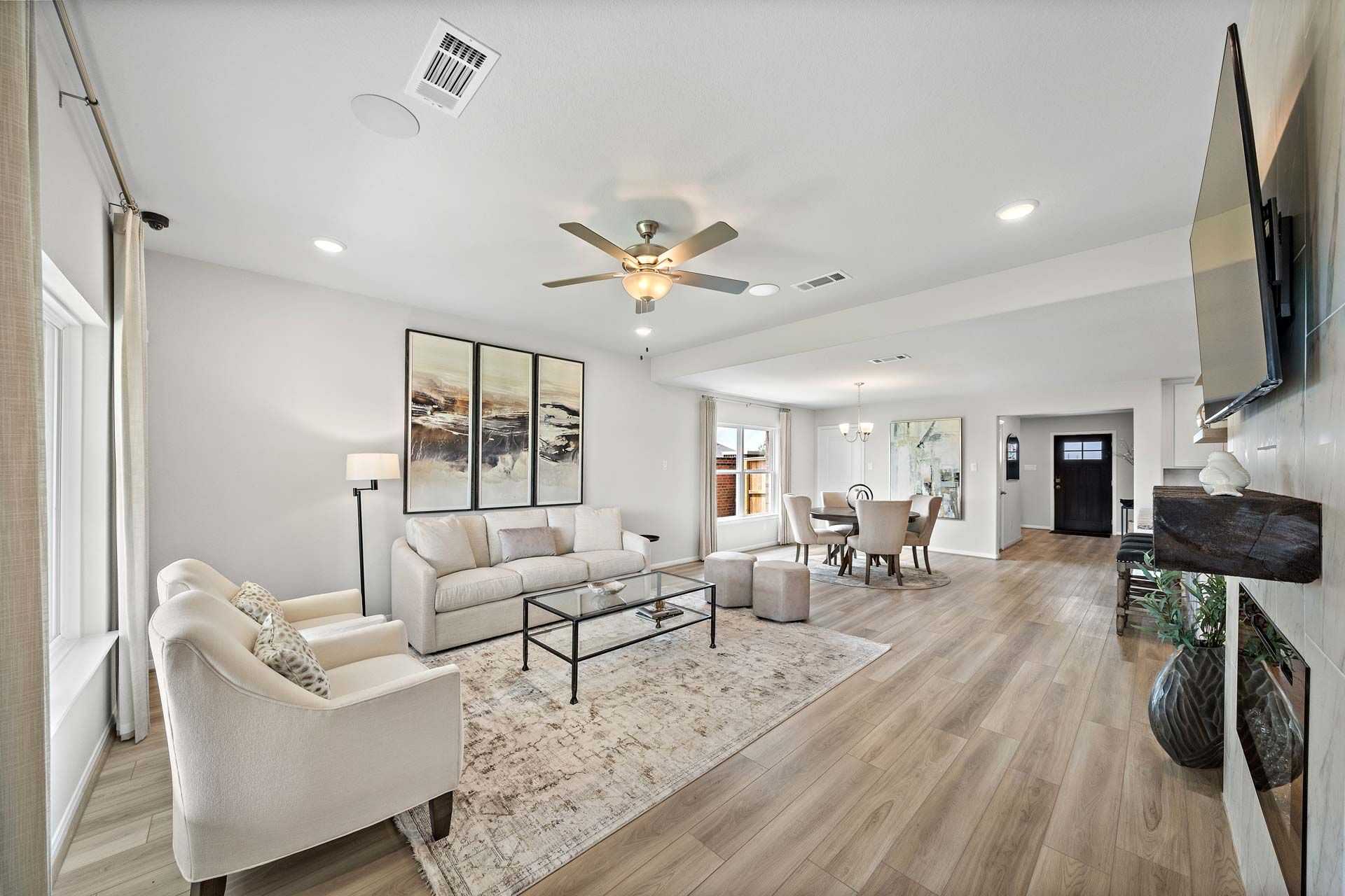 Open-concept living room at Enclave at Newport in Crosby Texas with beige sofa, ceiling fan, hardwood floors and dining area