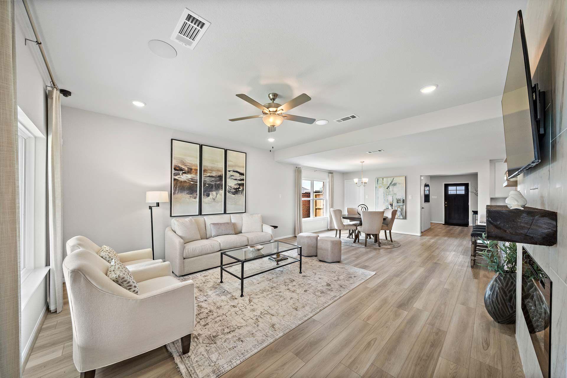 Open-concept living room at Enclave at Newport in Crosby Texas with beige sofa, ceiling fan, hardwood floors and dining area