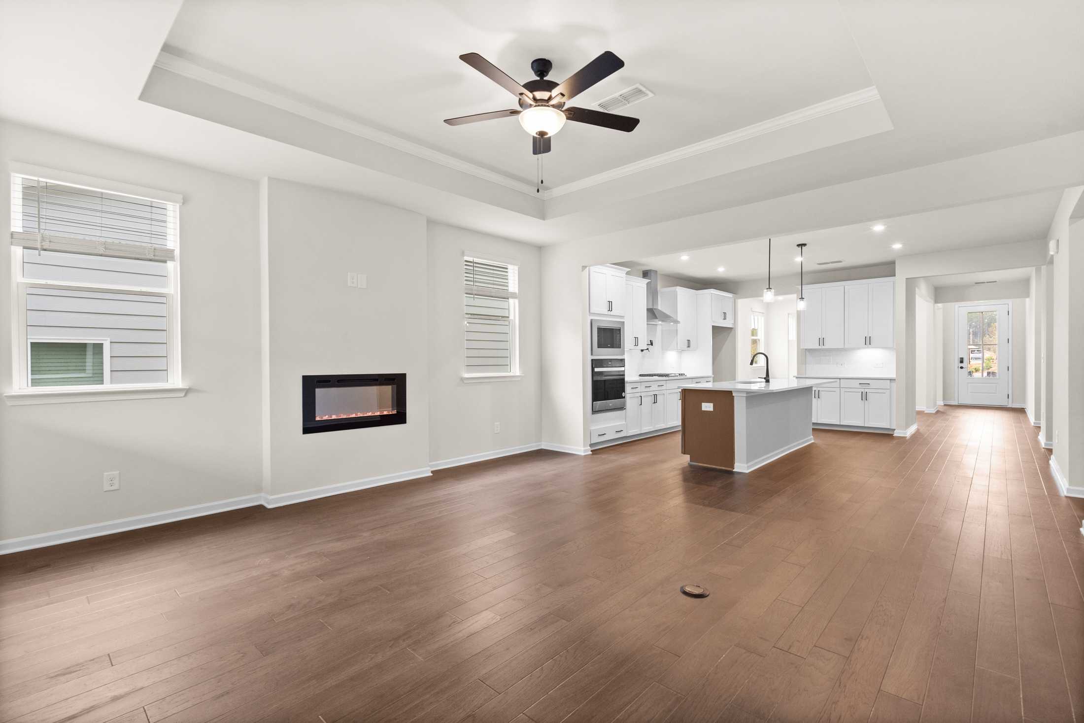 Open-concept kitchen and living area in The Glenwood B with white cabinetry, large island, linear fireplace, hardwood floors