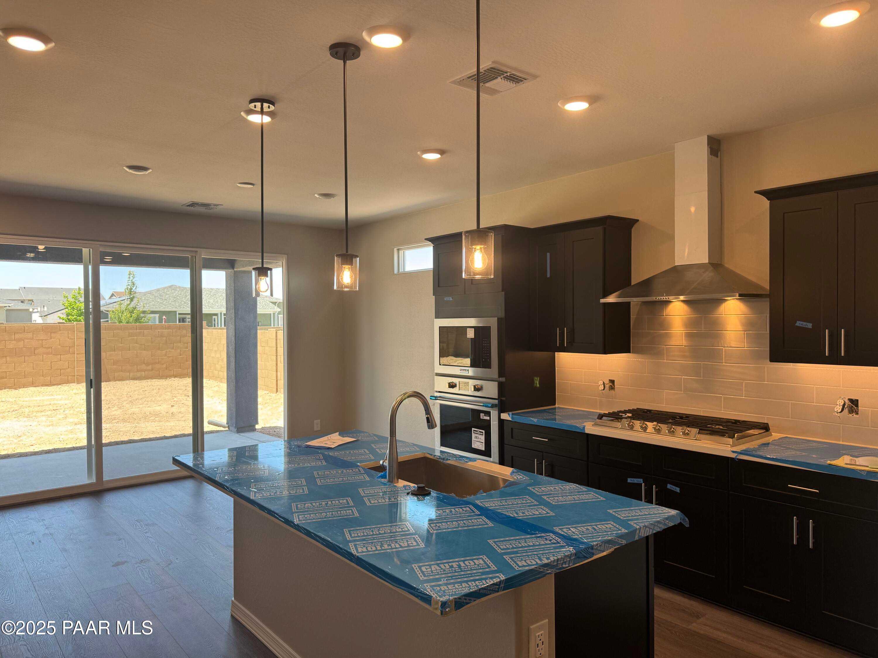 Modern kitchen with island, dark cabinets, stainless appliances, and sliding doors to desert backyard in Davidson Homes Durango II A, Prescott AZ