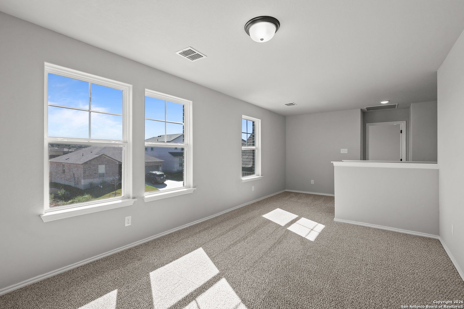 Bright upstairs loft with large windows overlooking neighborhood, bar counter, and carpeted flooring in The Murray K home, San Antonio