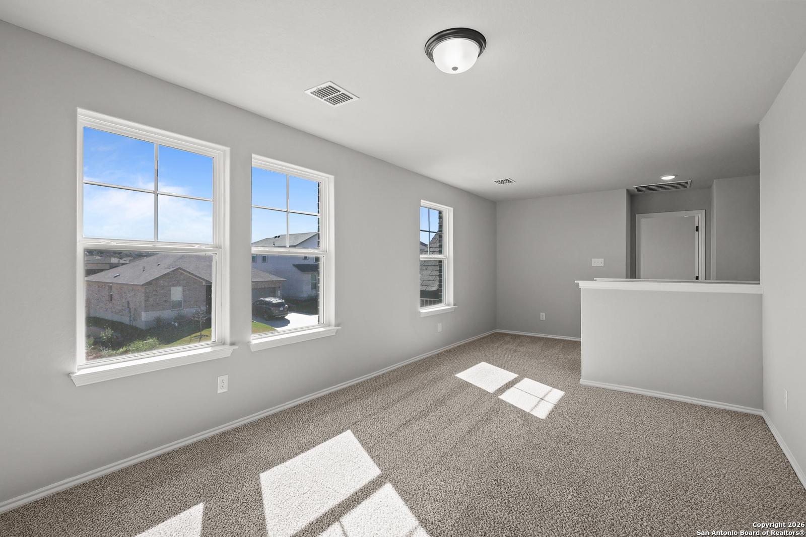 Bright upstairs loft with large windows overlooking neighborhood, bar counter, and carpeted flooring in The Murray K home, San Antonio
