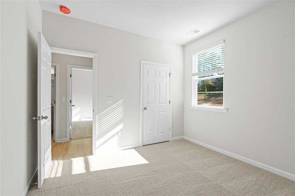 Bright secondary bedroom with neutral walls, carpet flooring, open doors, and window blinds in Davidson Homes The Glenwood C, Hoschton, Georgia