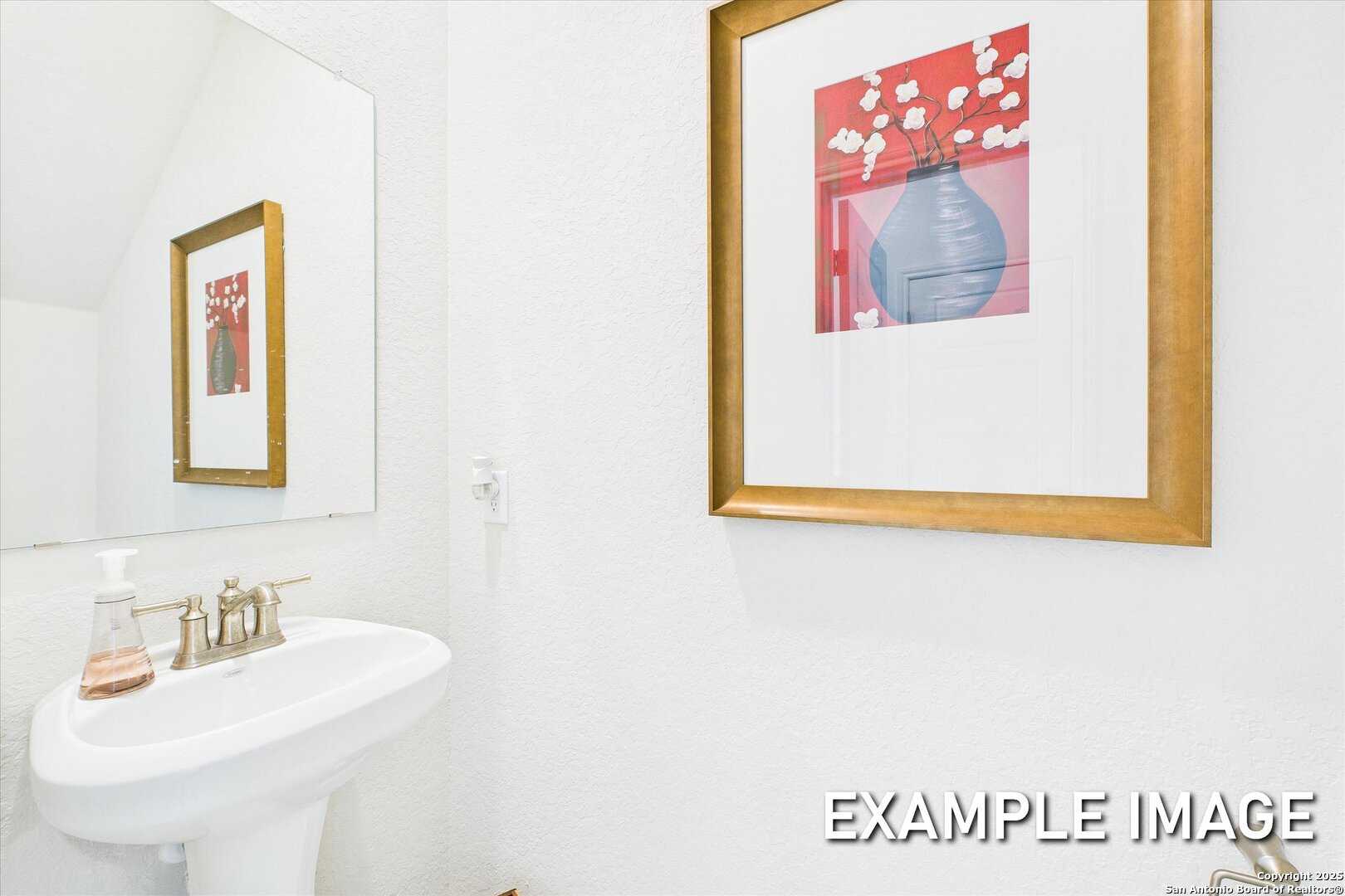 Bright powder room with white pedestal sink, framed mirror, and abstract red floral art in Davidson Homes The Brazos C, San Antonio