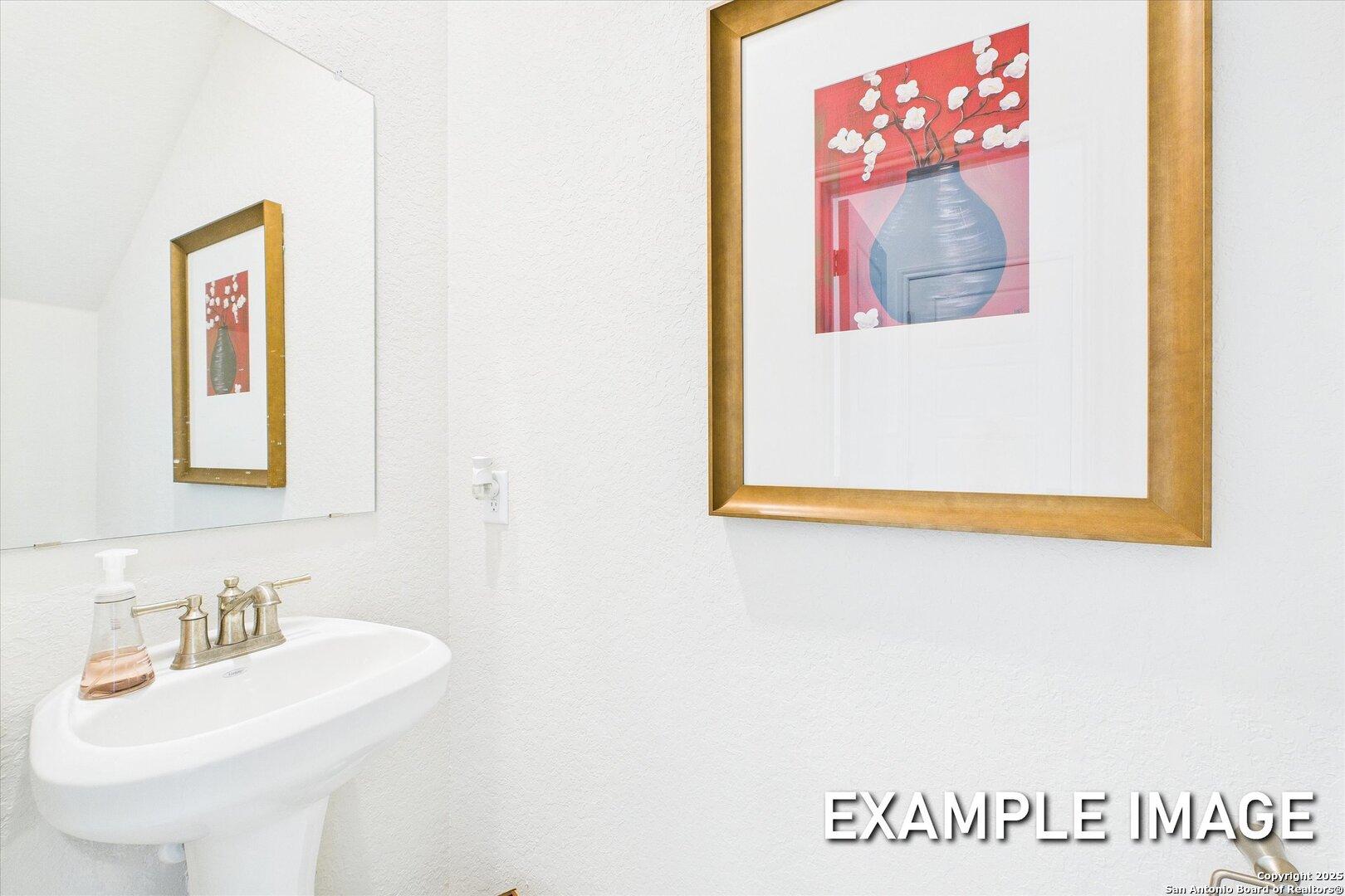 Elegant powder room with white pedestal sink, gold faucet, and abstract red-blue wall art in Davidson Homes The Brazos C, San Antonio