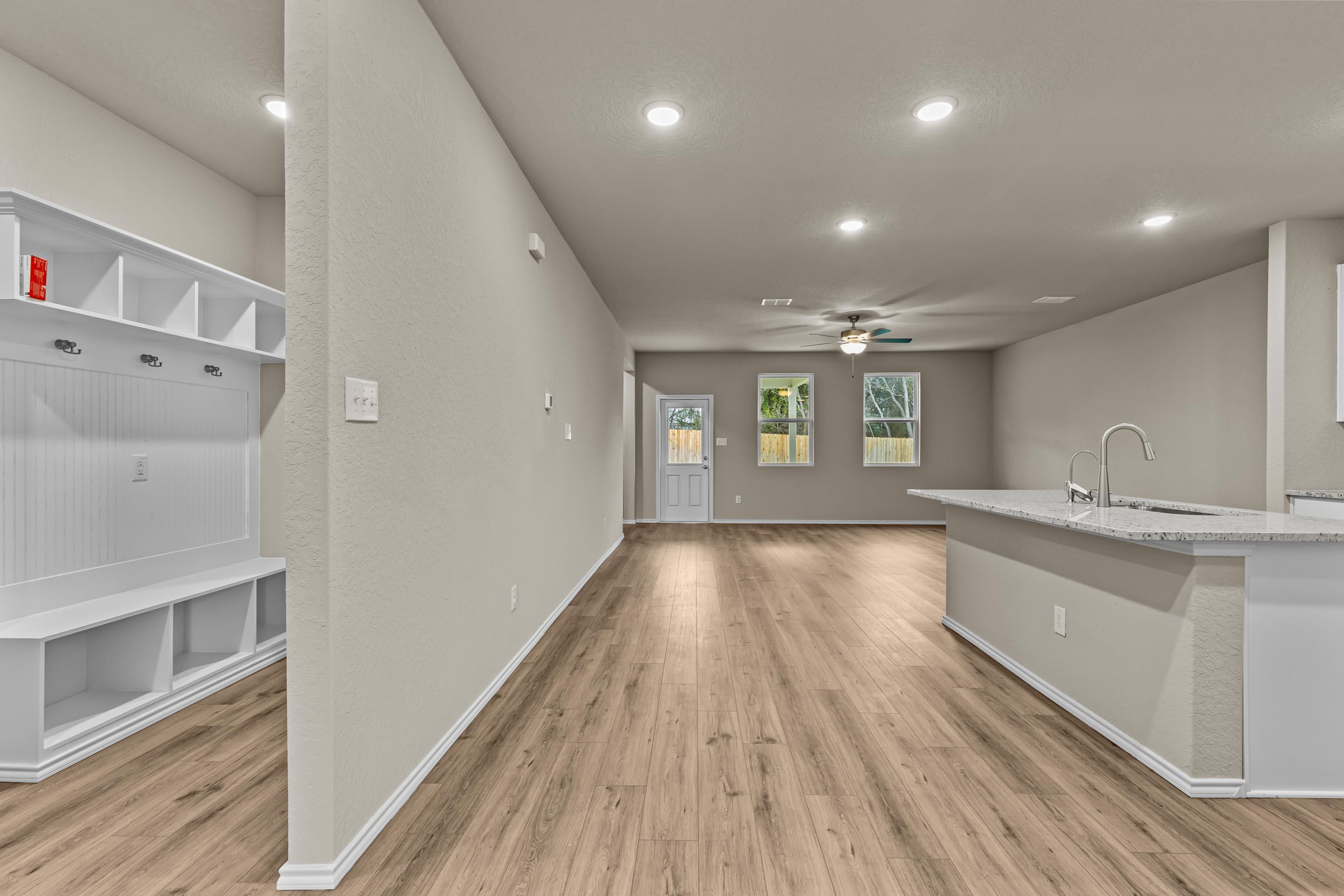 Spacious mudroom with white built-in cabinets, hardwood floors, and open kitchen island in Davidson Homes The Douglas F, San Antonio