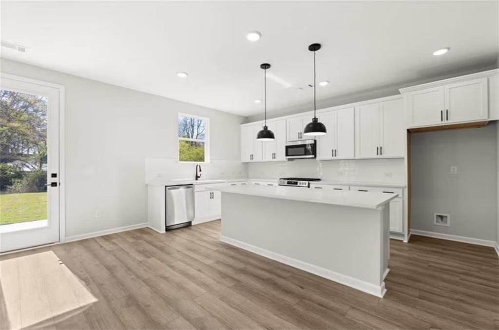 Bright modern kitchen with white shaker cabinets, stainless appliances, island, and backyard view in The Hickory B, Winder, GA