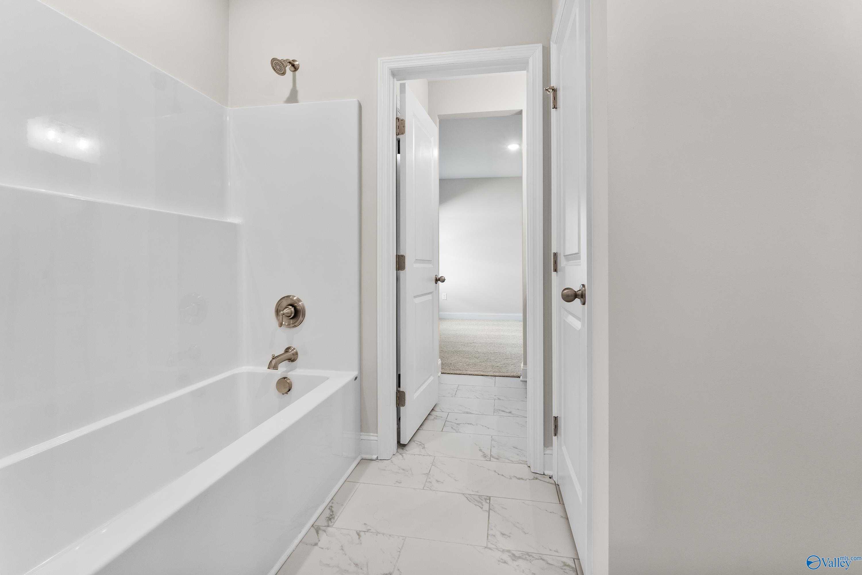 Modern guest bathroom with white tub-shower combo, subway tile walls, and marble-look floor in Davidson Homes The Finleigh, Toney, Alabama
