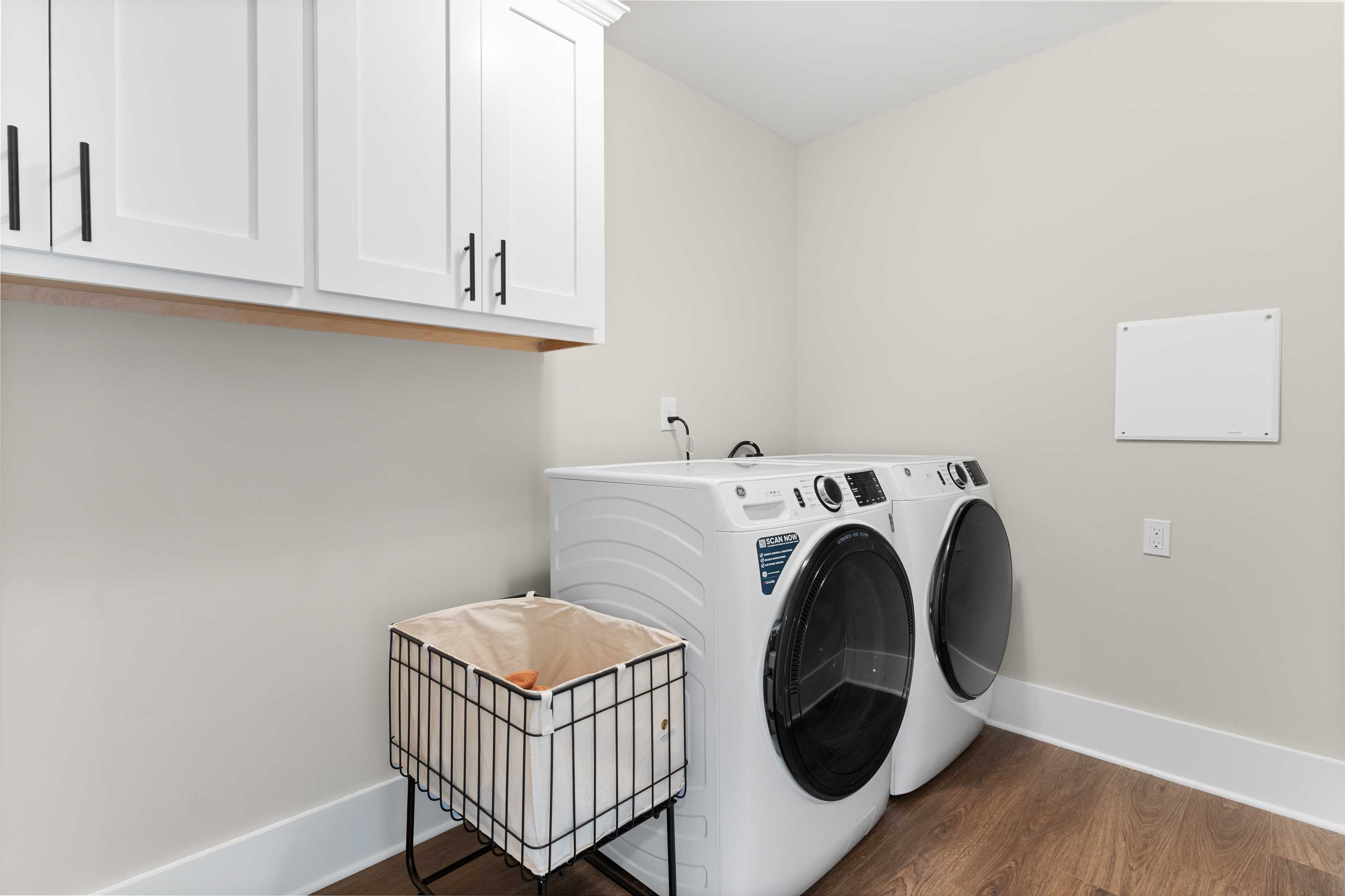 Spacious laundry room in The Shelby A Davidson Homes design featuring white washer, dryer, cabinets, sink, and hardwood floors