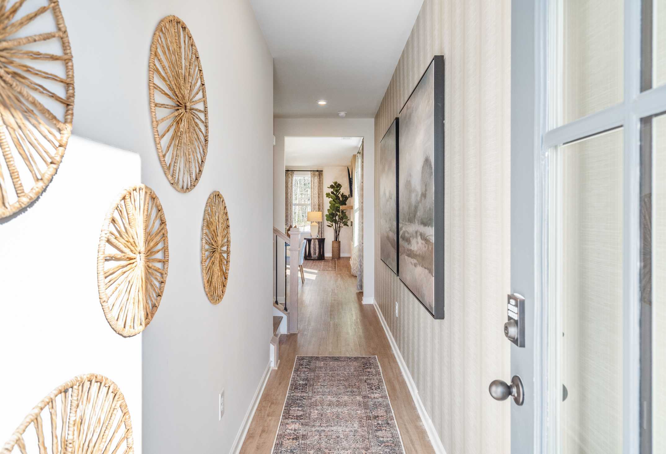 Spacious hallway in The Marion A Davidson Homes with woven wall decor, striped wallpaper, large framed art, and hardwood floors