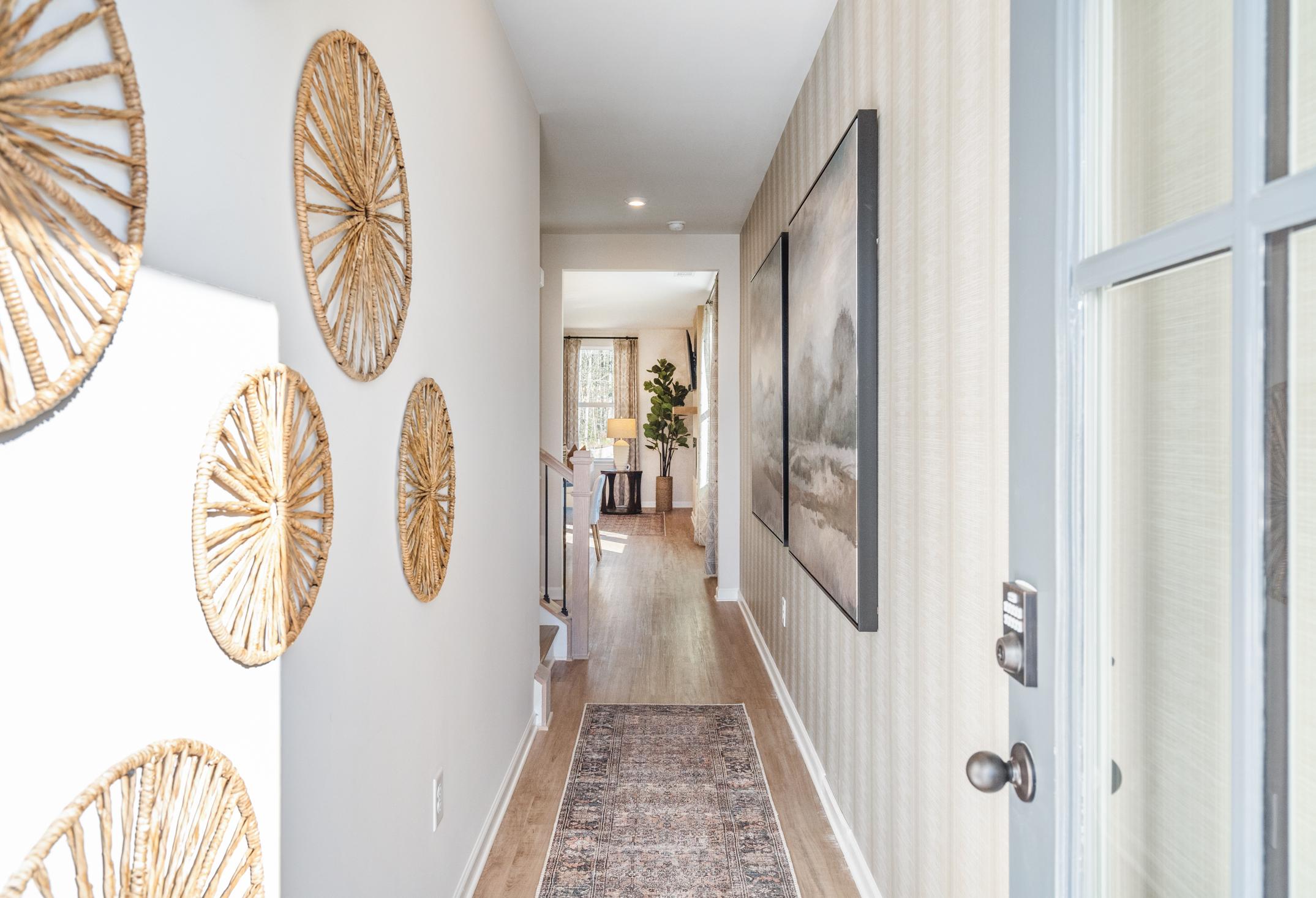 Spacious hallway in The Marion A Davidson Homes with woven wall decor, striped wallpaper, large framed art, and hardwood floors
