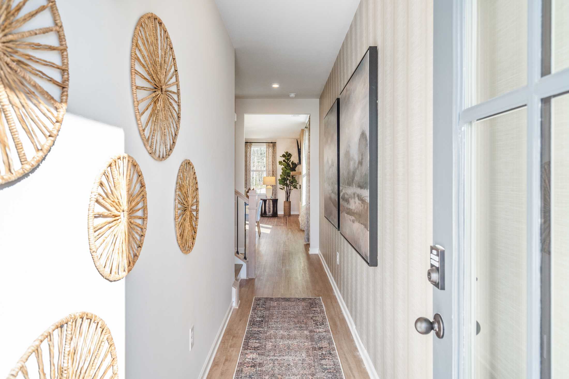 Spacious hallway in The Marion B home design with woven rattan wall decor, hardwood floors, and striped wallpaper