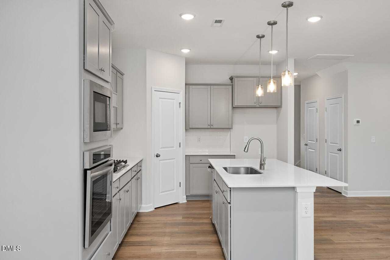 Modern kitchen with gray cabinets, stainless appliances, white island, and pendant lights in Davidson Homes The Warren, Fuquay-Varina, NC