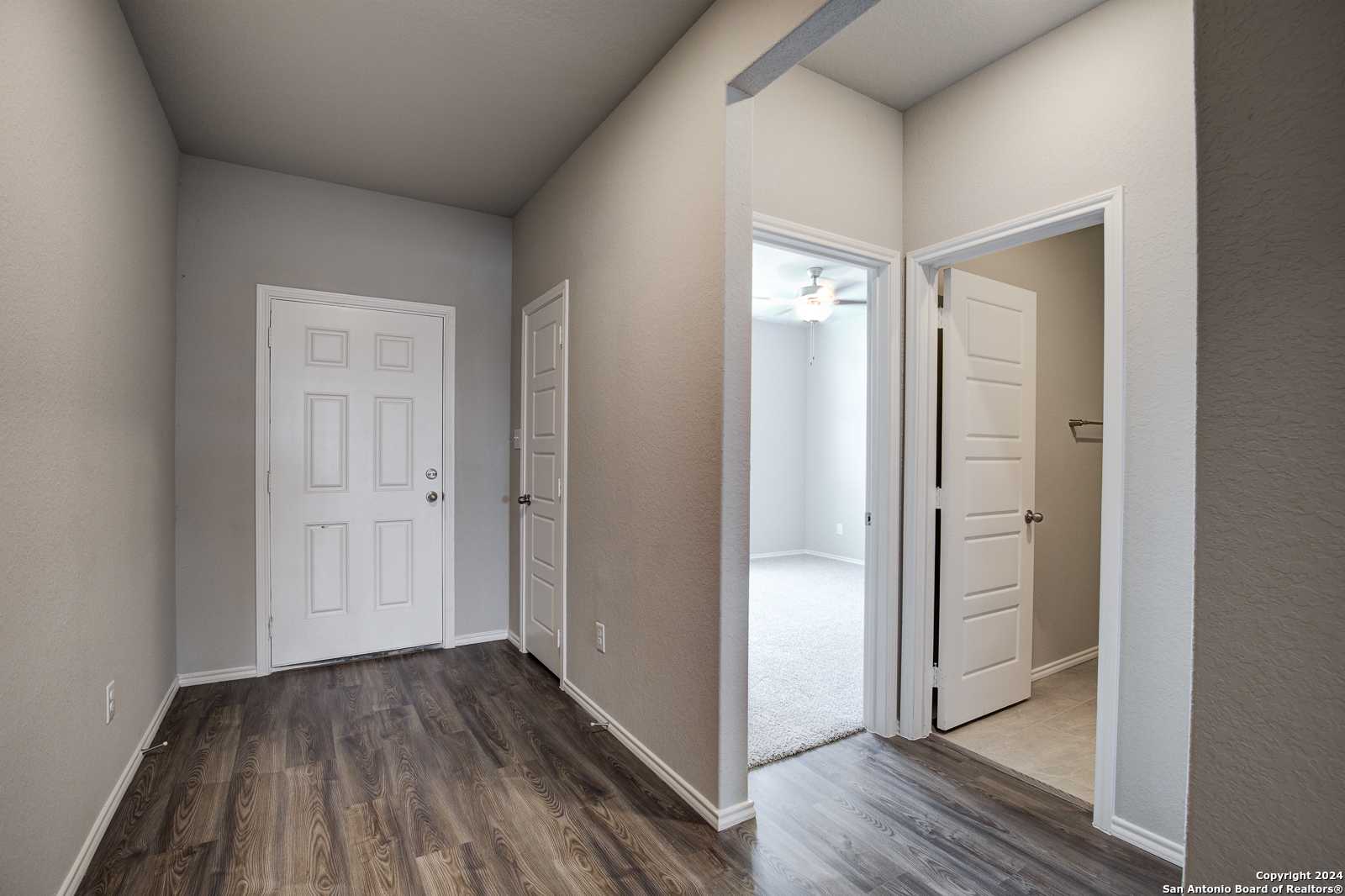 Spacious hallway with hardwood floors, white doors, and carpeted bedroom featuring ceiling fan in The Daphne J home, Seguin, Texas