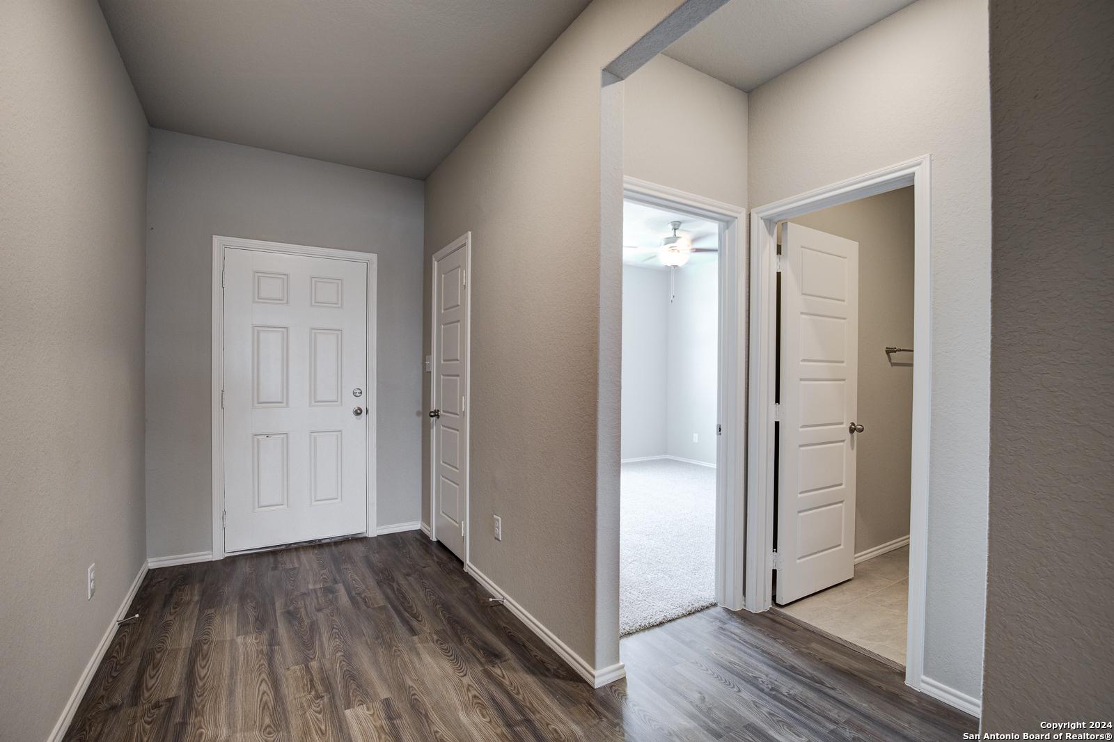 Spacious hallway with hardwood floors, white doors, and carpeted bedroom featuring ceiling fan in The Daphne J home, Seguin, Texas