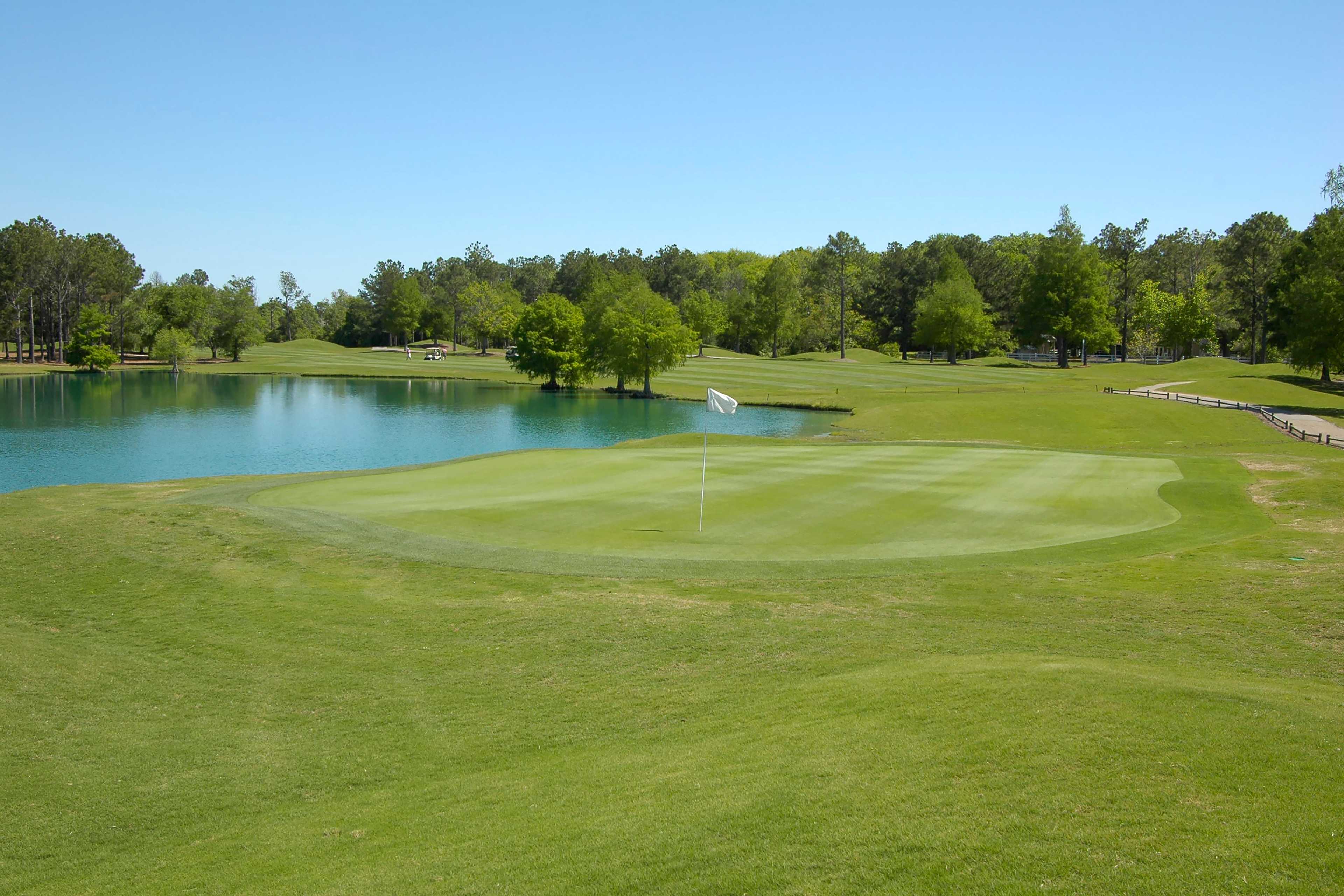 Lush golf green and fairway at Little Creek in Arab, Alabama with pond, flagstick and tree-lined backdrop