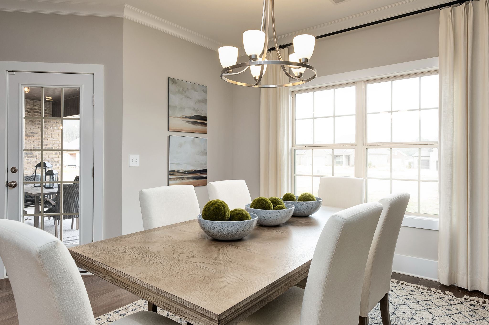 Elegant dining room in Chimney Creek Hampton Cove Alabama with wooden table, white chairs, moss ball centerpieces, chandelier, and large windows