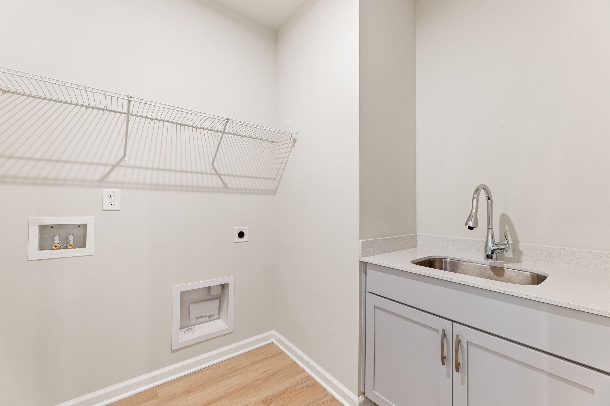 Modern laundry room with utility sink, wire shelving, and washer/dryer hookups in Davidson Homes The Glenwood C, Loganville, GA