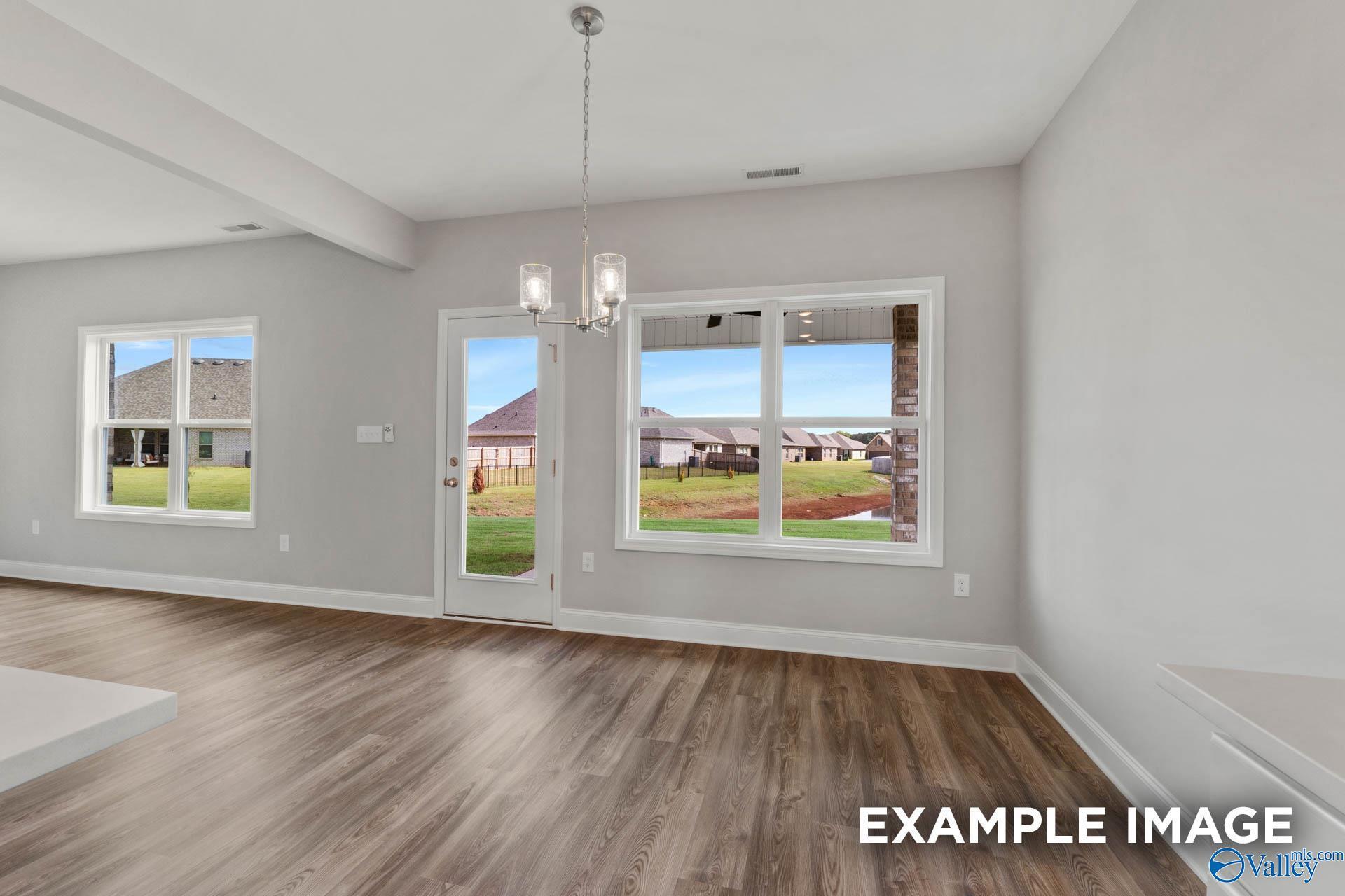 Spacious living room with hardwood floors, chandelier, and large windows to grassy backyard in 4-bedroom Shelby B home, Heritage Lakes, New Market, AL