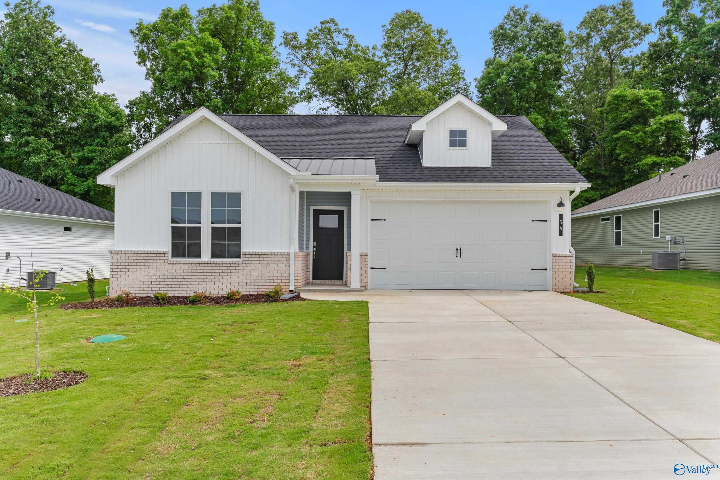 Charming 1-story white home with black roof, 2-car garage, brick accents, concrete driveway, lush green lawn and trees in Bailey Park, Fayetteville, Tennessee
