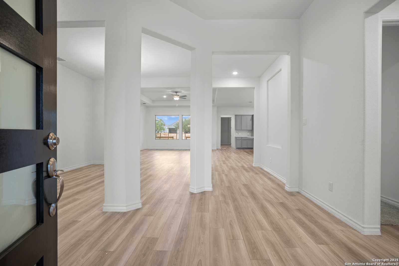 Grand entryway with dark wood door, white columns, and open layout in Davidson Homes The Summerlin B, Castroville, Texas