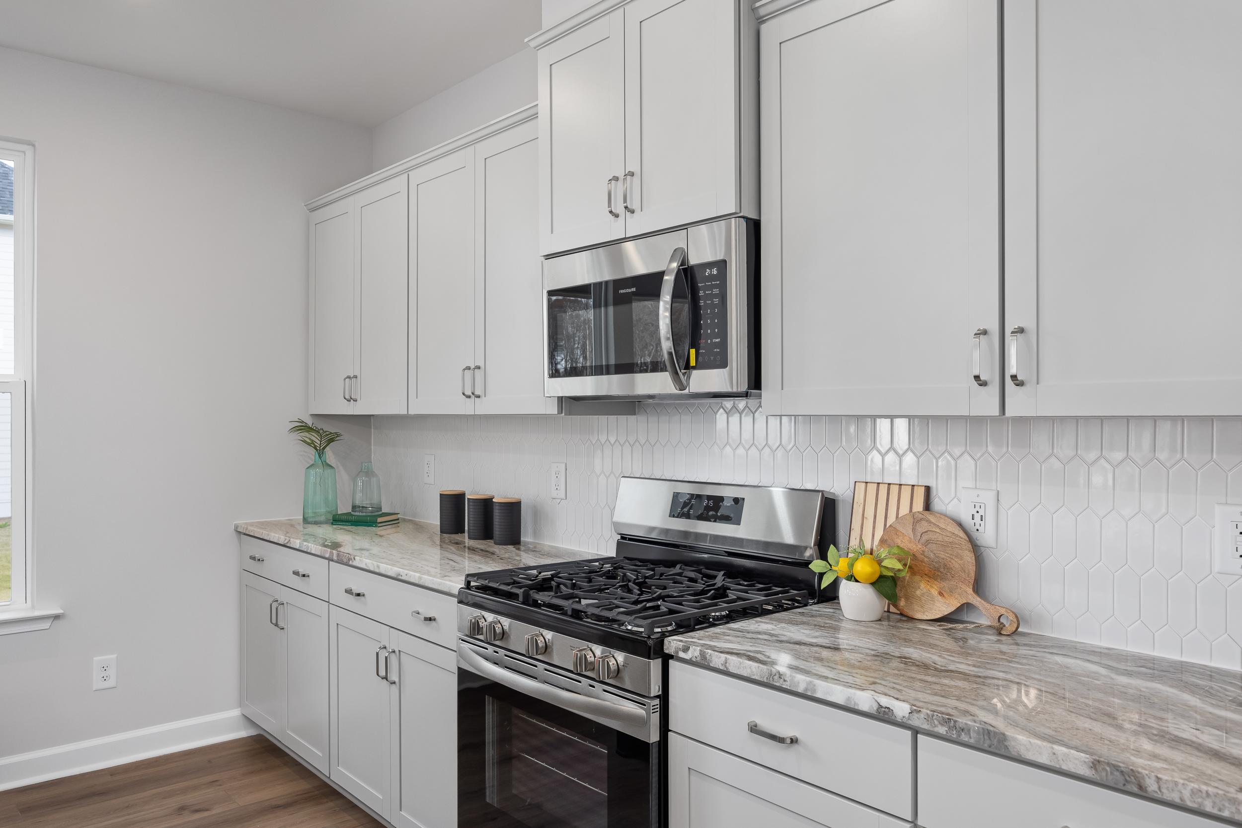 Modern white shaker kitchen at Enclave at Belmont in Belmont NC with stainless steel appliances, quartz counters, herringbone backsplash