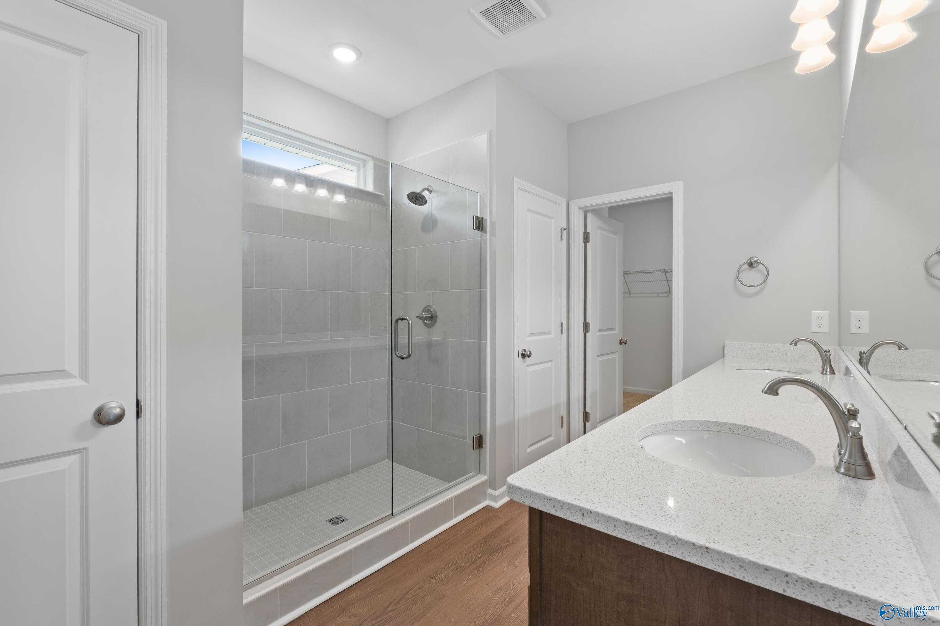 Modern master bathroom featuring frameless glass shower, double quartz vanity, and hardwood floors in Davidson Homes The Stella, Hazel Green, Alabama