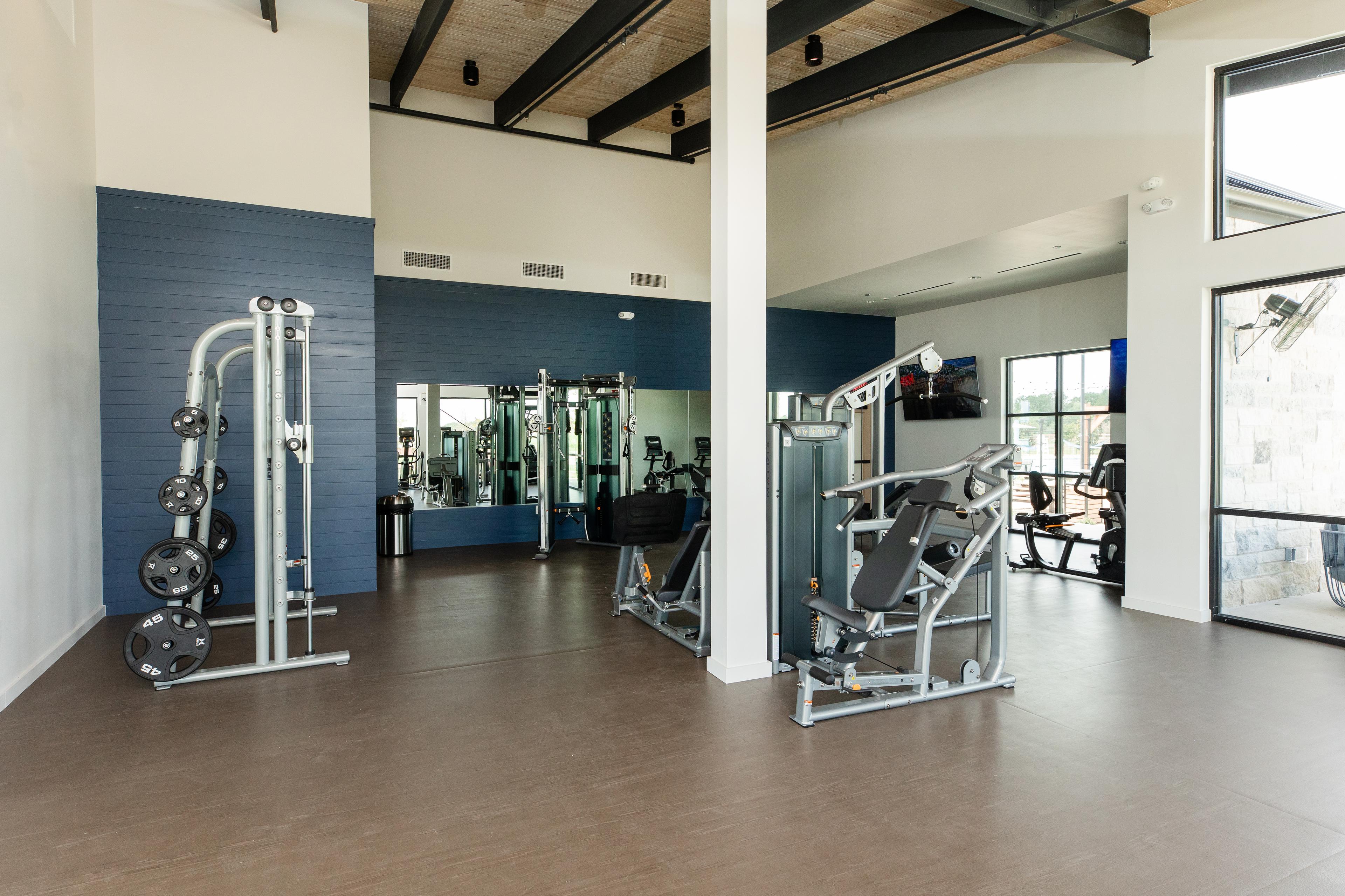 Spacious fitness center at Emberly in Beasley Texas with exposed wooden beams, blue accent wall, mirrors, and weight machines
