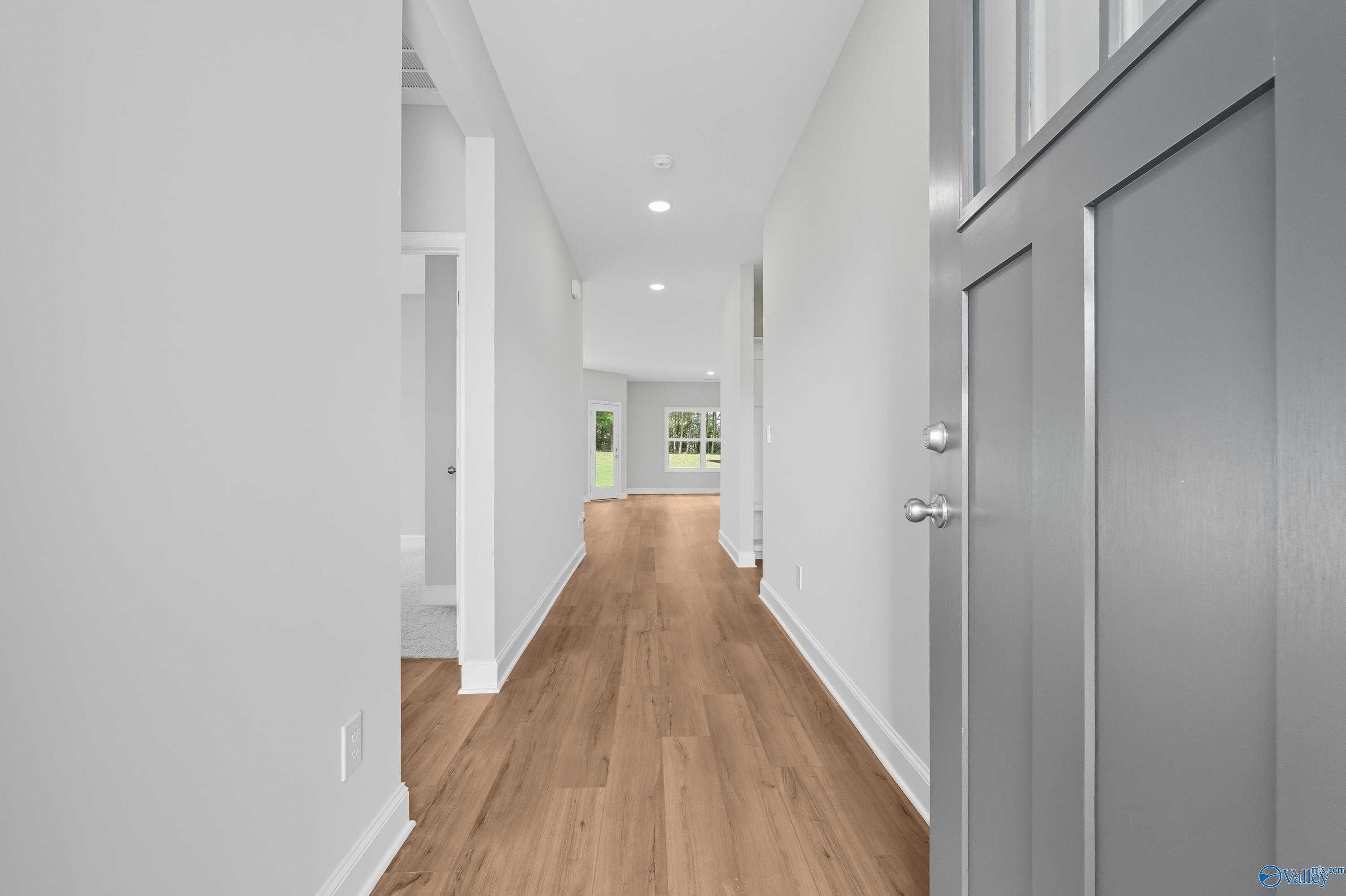 Bright hallway with light hardwood floors, white walls, and open doorway to backyard view in The Franklin C home, Meridianville
