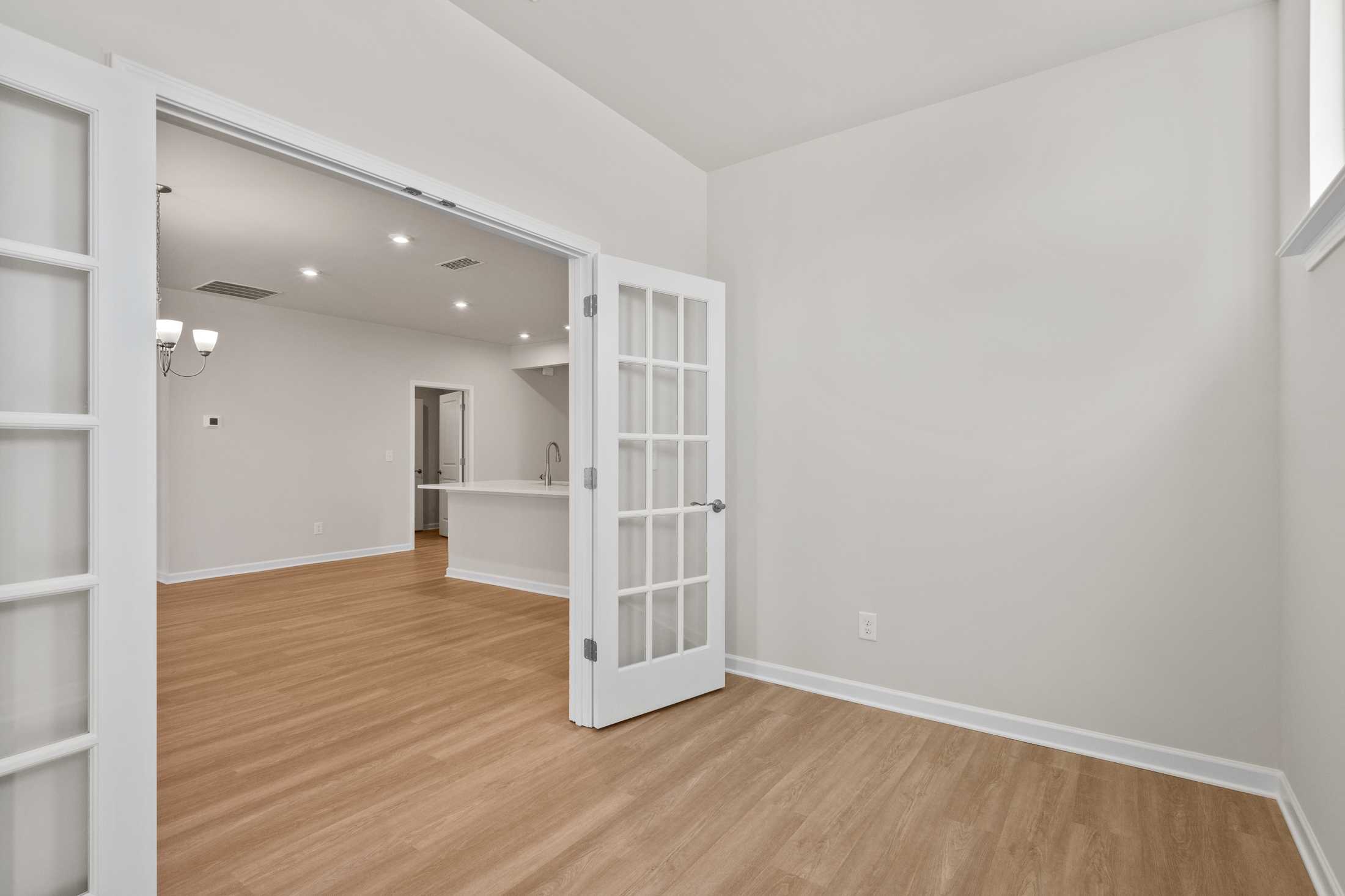 Spacious The Dawson C interior with open white French doors revealing modern kitchen island and light hardwood floors in Loganville GA home