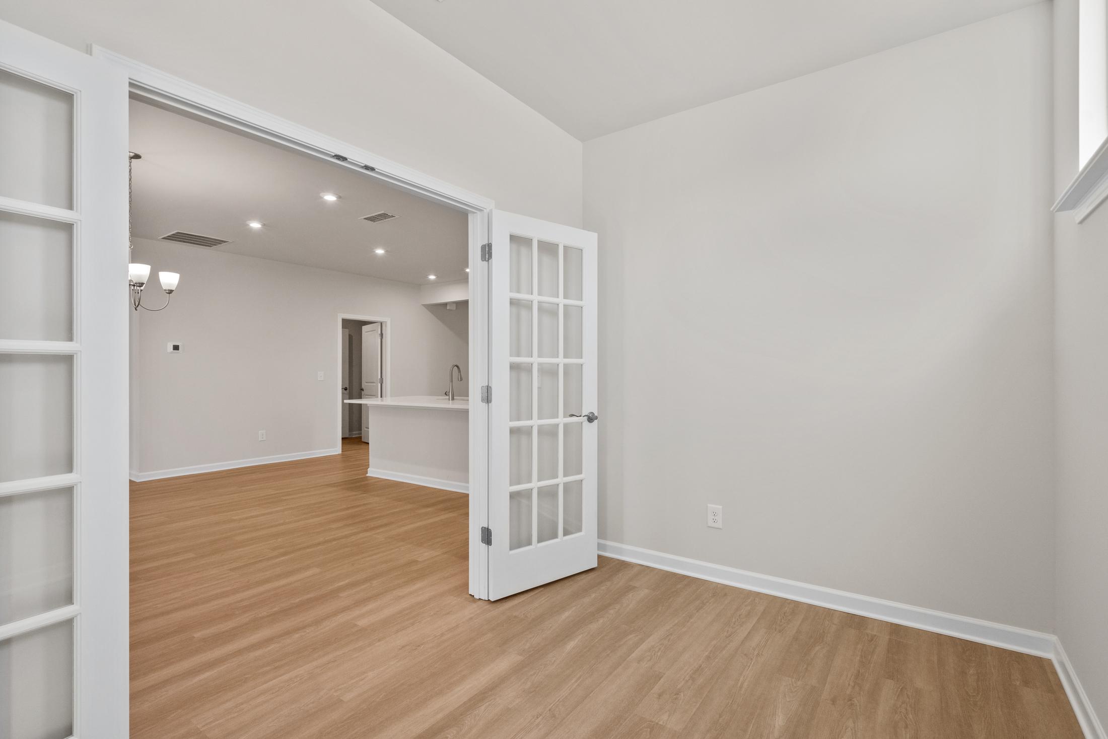 Spacious The Dawson C interior with open white French doors revealing modern kitchen island and light hardwood floors in Loganville GA home