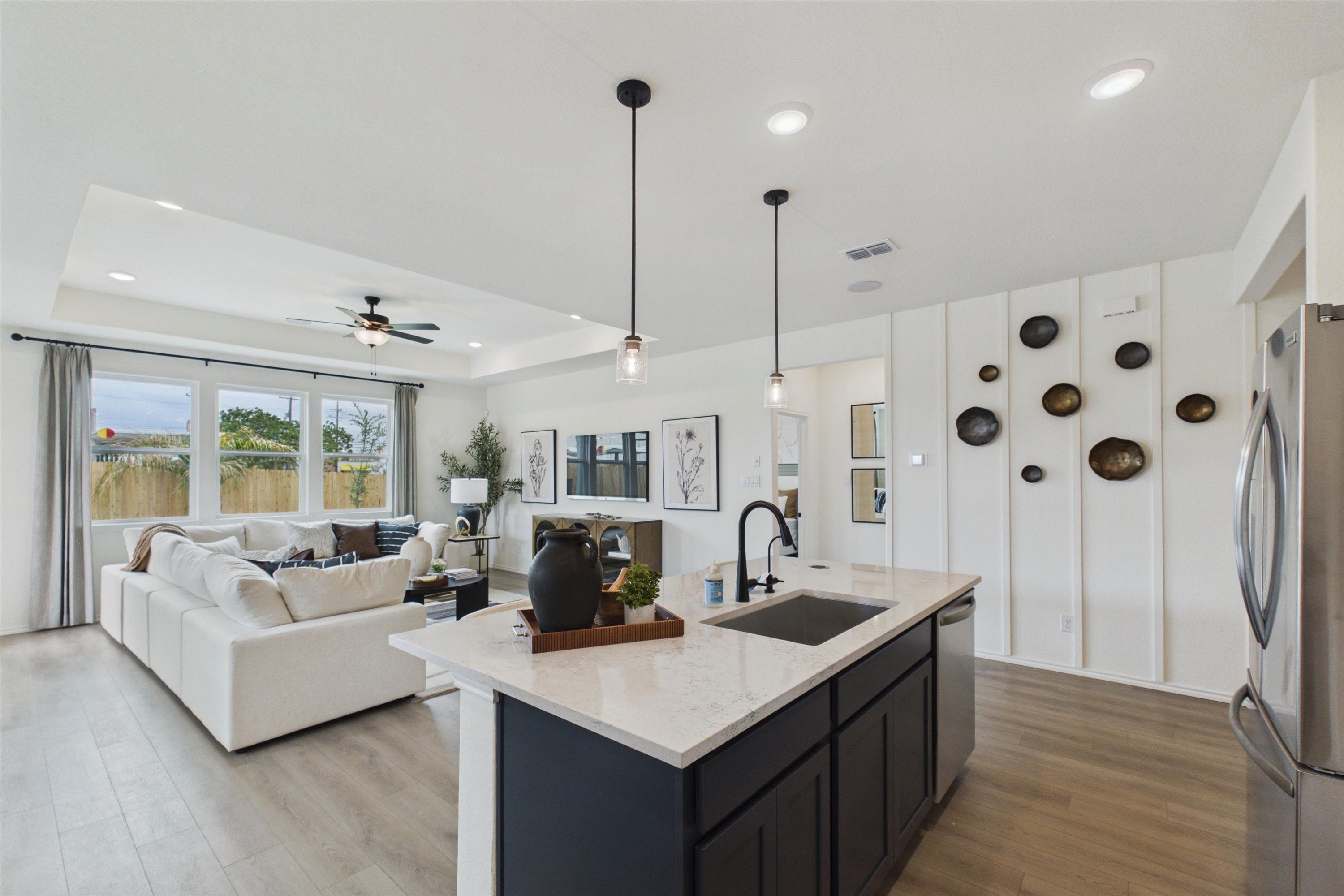 Open-concept kitchen living room at Rayburn Valley San Antonio TX by Davidson Homes with white quartz island, L-shaped sofa, hardwood floors