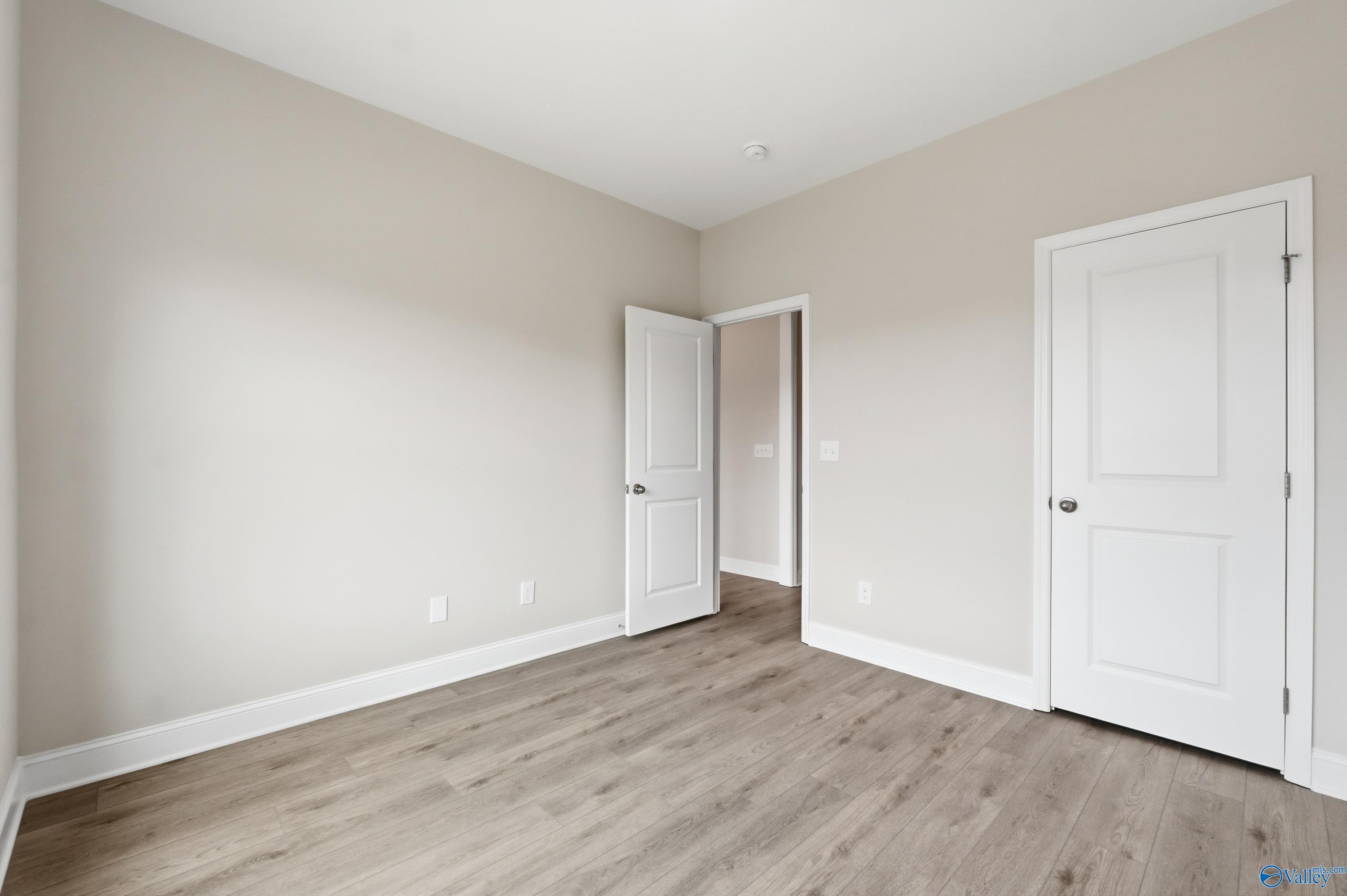Spacious secondary bedroom with beige walls, white doors, open hallway access, and luxury vinyl plank flooring in Davidson Homes The Shelby B, New Market, Alabama