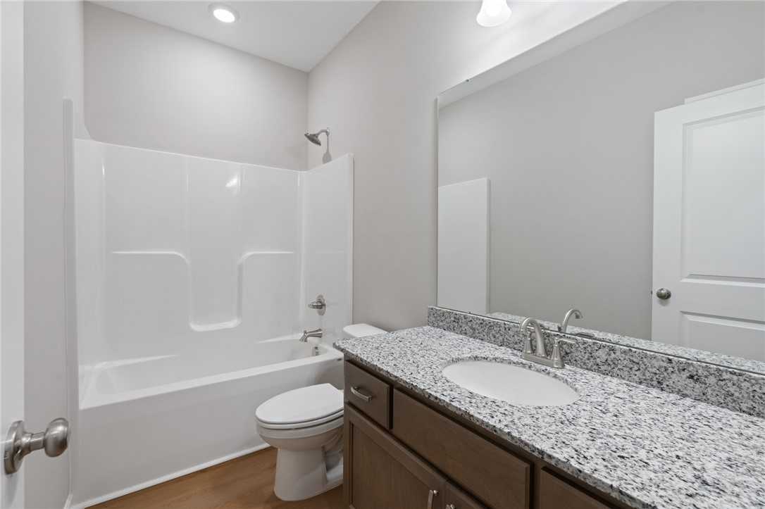 Modern guest bathroom featuring granite vanity, white tub-shower combo, and wood floors in Davidson Homes The Luna B, Opelika, Alabama