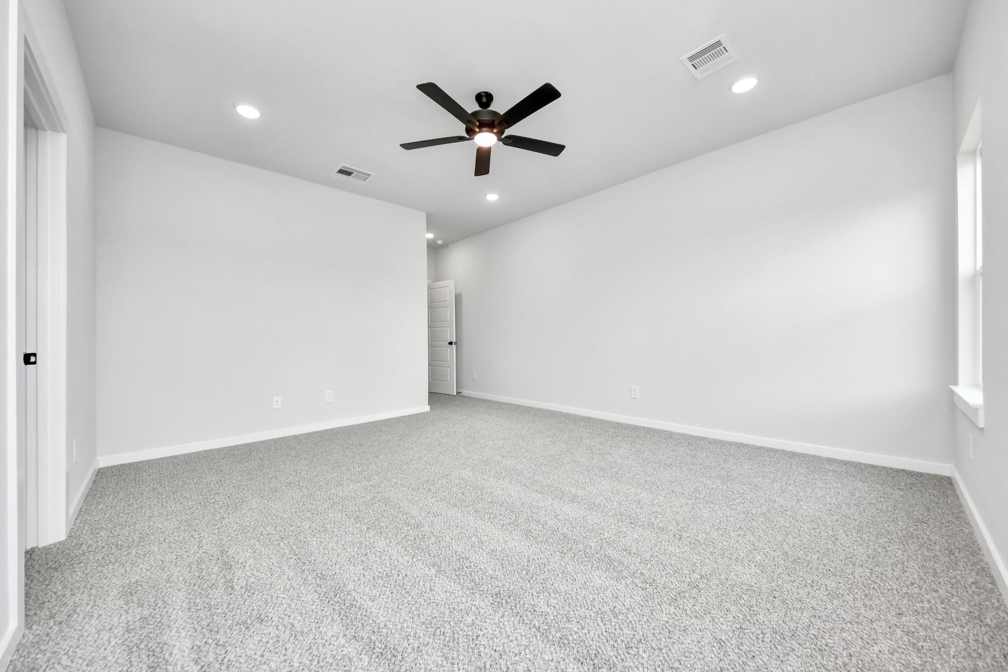 Spacious, neutral-toned bedroom with ceiling fan in The Sorrento E floor plan at Sundance Cove in Crosby, Texas.