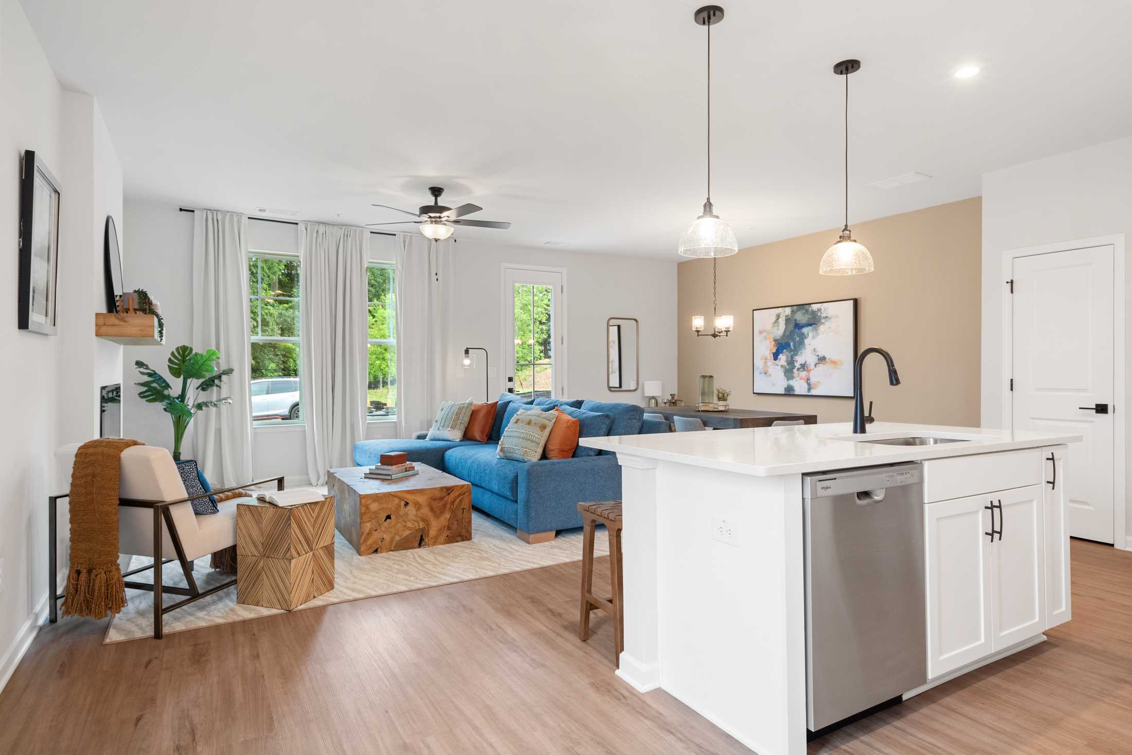 Open-concept living room and kitchen at Rosehill Townhomes in Marietta GA with blue sofa, hardwood floors, white island, and pendant lights