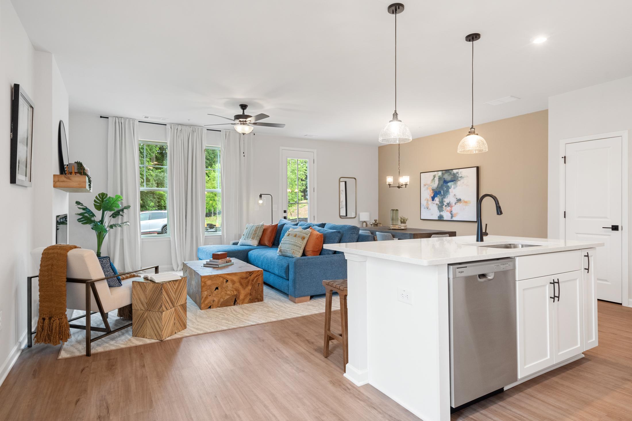 Open-concept living room and kitchen at Rosehill Townhomes in Marietta GA with blue sofa, hardwood floors, white island, and pendant lights