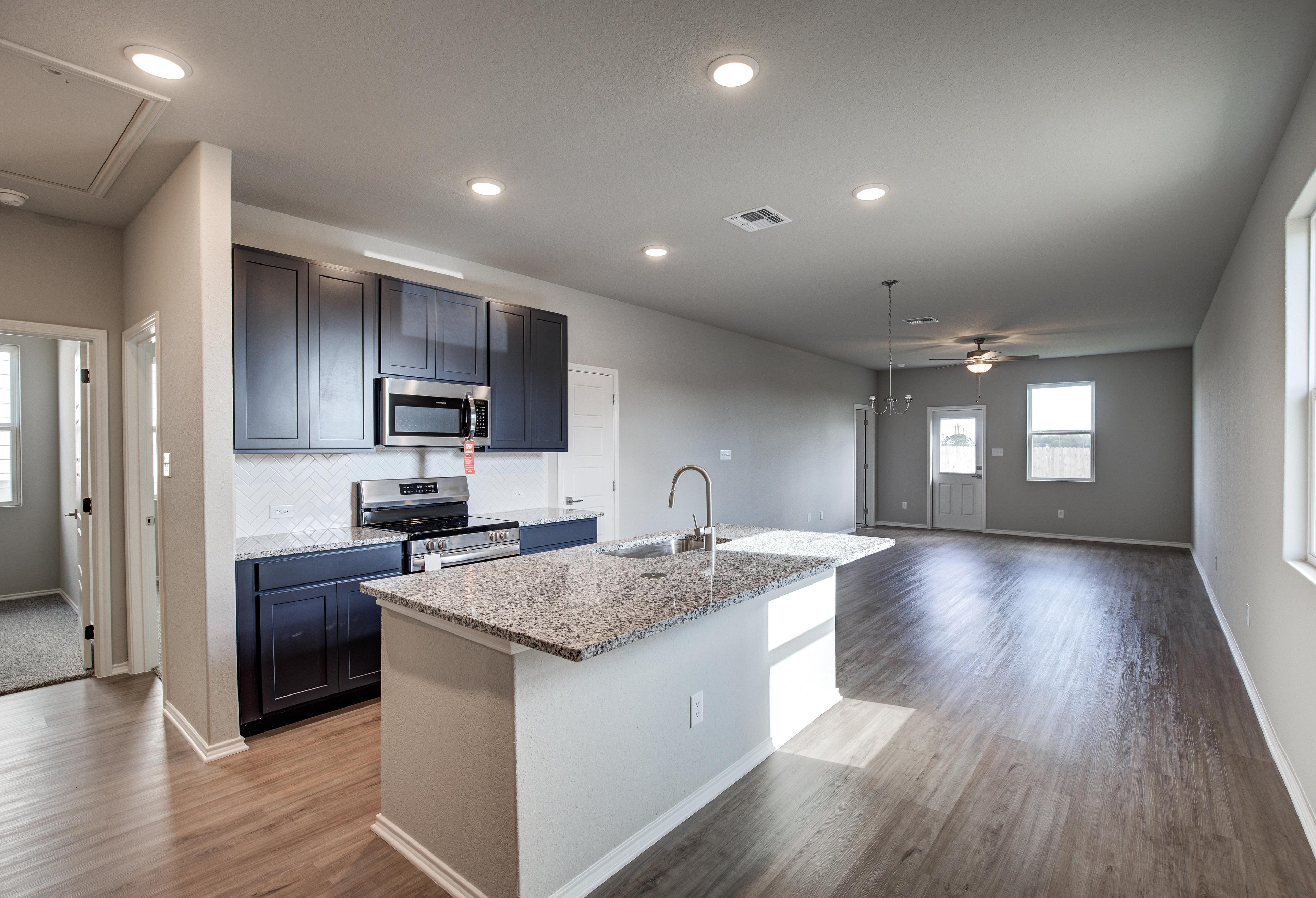 Modern kitchen in The Frio home design by Davidson Homes featuring dark cabinets, granite island, and open living area
