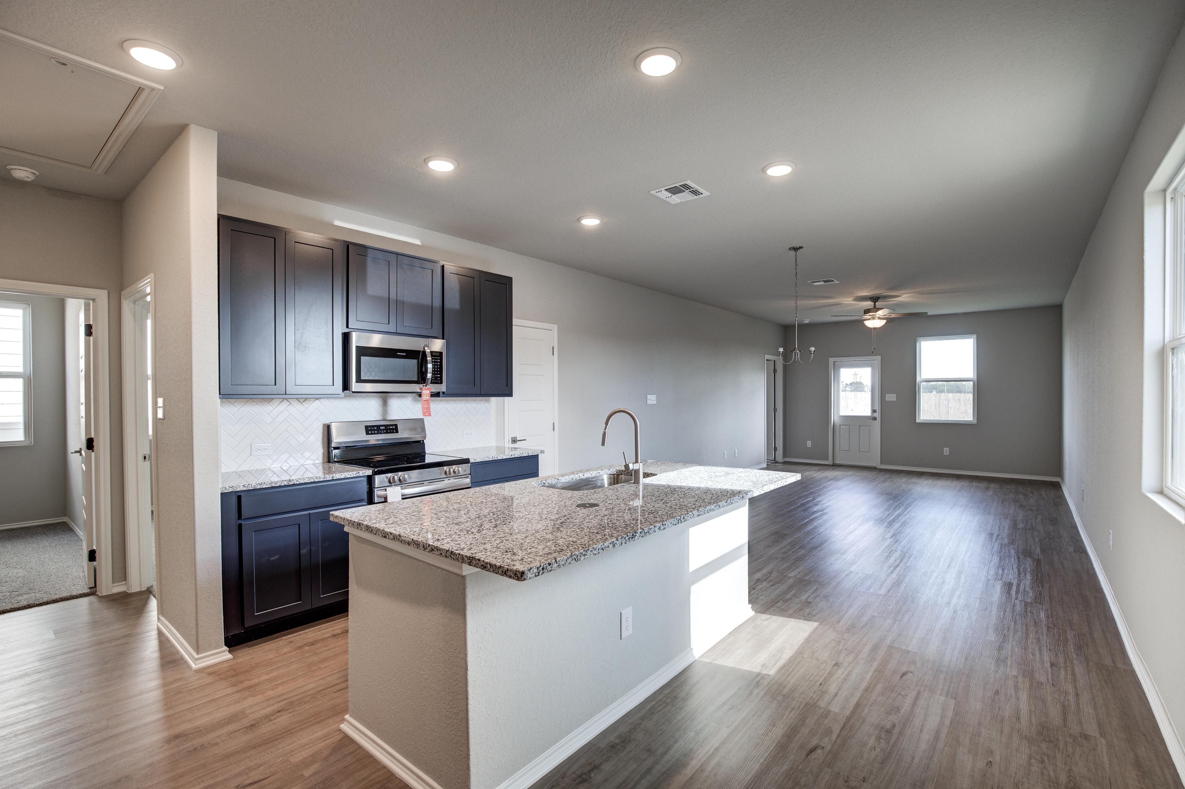Open-concept kitchen in The Frio showcasing dark cabinets, granite island, stainless appliances, and adjacent living space