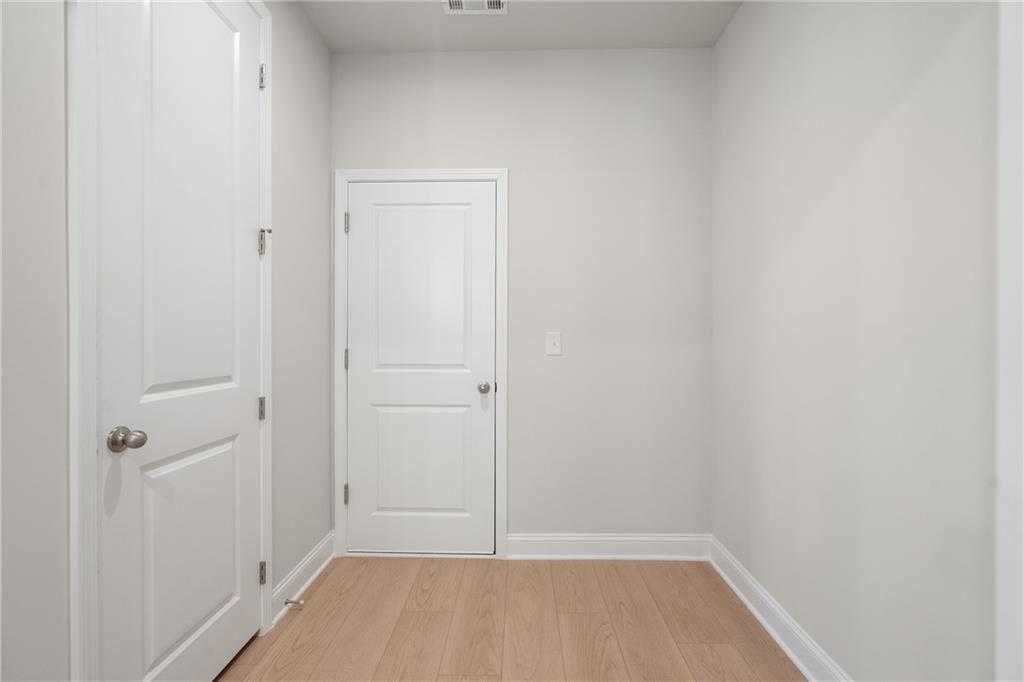 Bright hallway featuring white doors, light gray walls, and oak hardwood floors in The Hickory E 4-bedroom home, Buford, Georgia