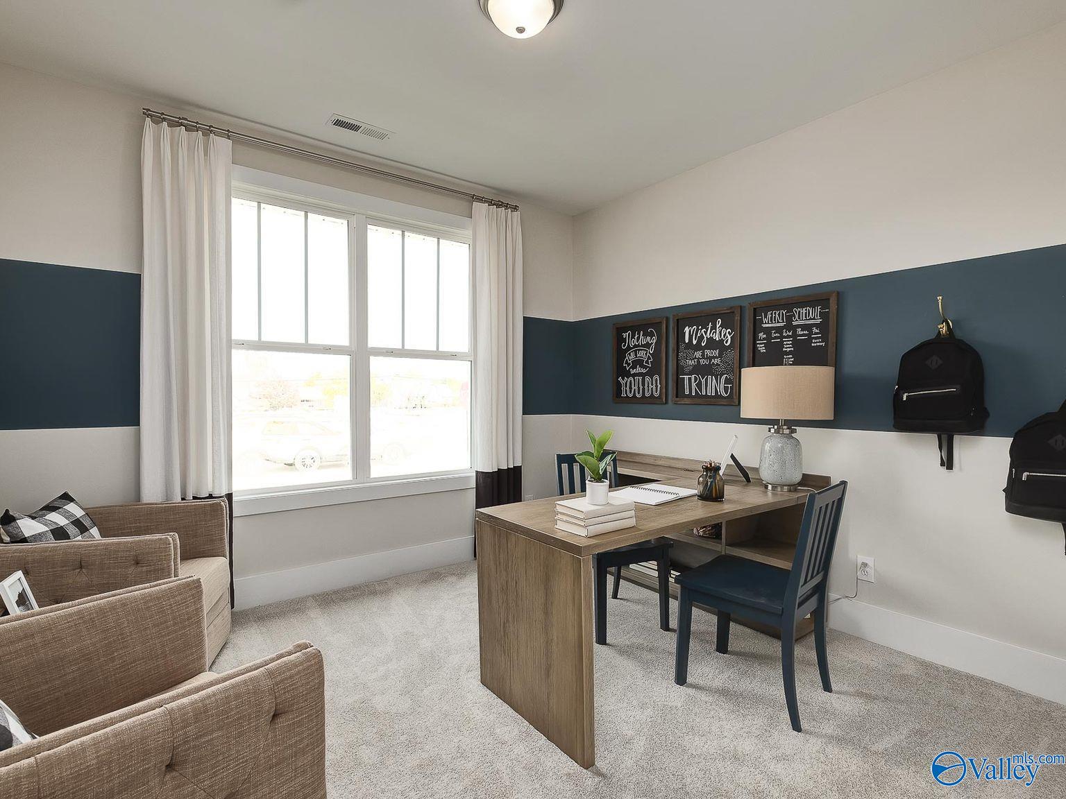 Cozy home office with wooden desk, navy accent wall, large window, and armchairs in Davidson Homes The Everett, Toney, Alabama
