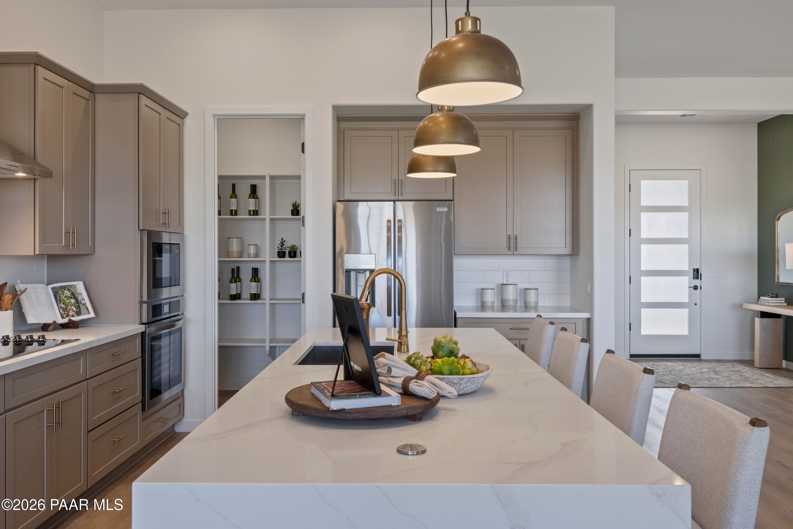 Modern kitchen island with quartz countertops, brass pendant lights, and walk-in pantry in The Blaze D home, Prescott, AZ.