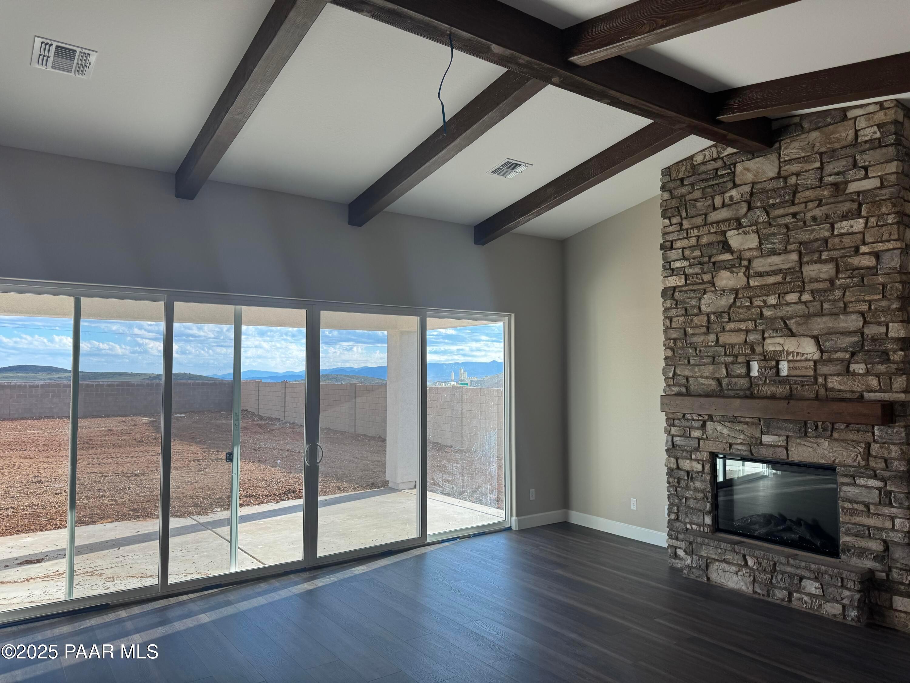 Bright living room with stone gas fireplace, exposed wood beams, and sliding doors to desert mountain views in Evermore Homes The Sunrise A, Prescott Valley, AZ