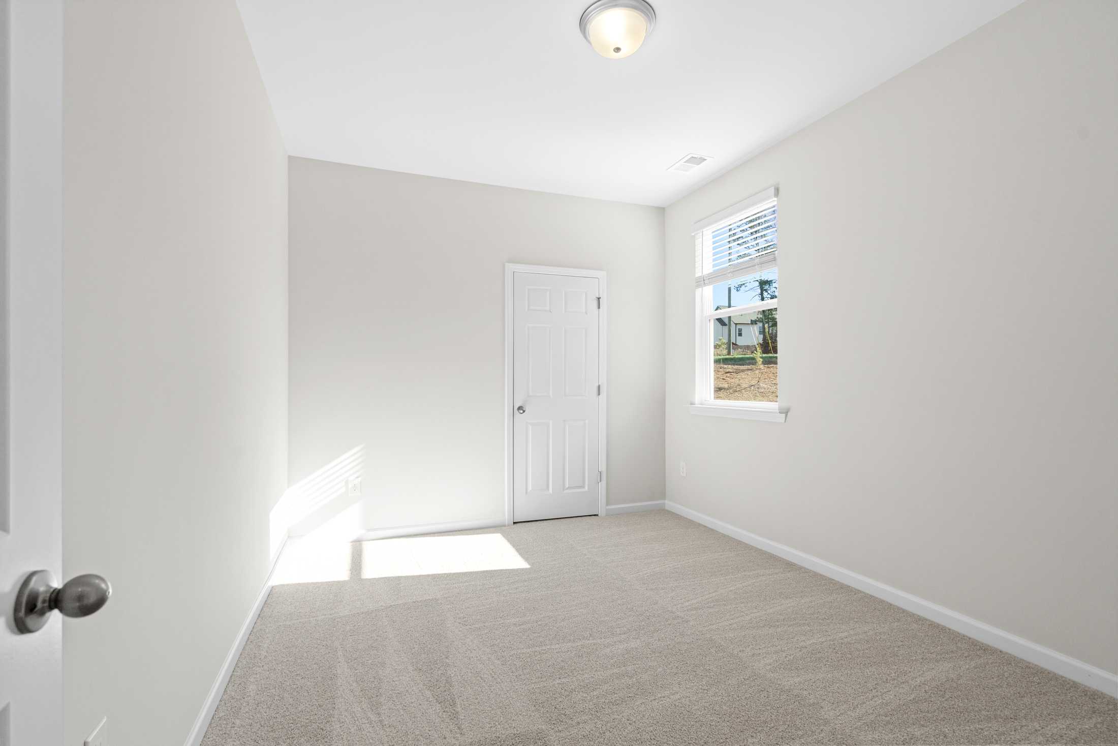 Spacious secondary bedroom in The Glenwood A at Wehunt Meadows, Hoschton GA: neutral walls, beige carpet, large window