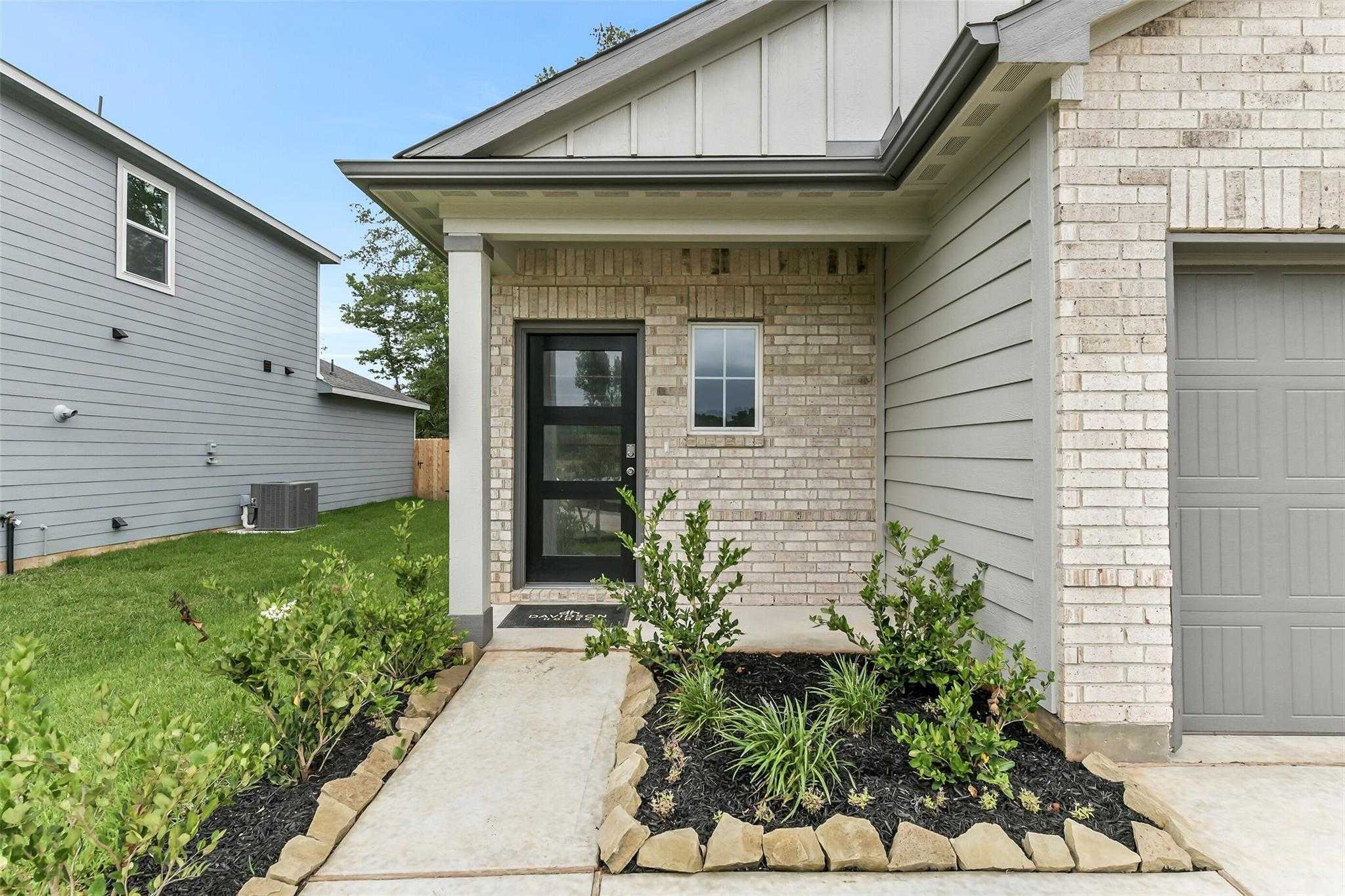 Charming brick and siding entryway with black door, covered porch, lush landscaping, and 2-car garage in Davidson Homes The Sabine F, Conroe, Texas