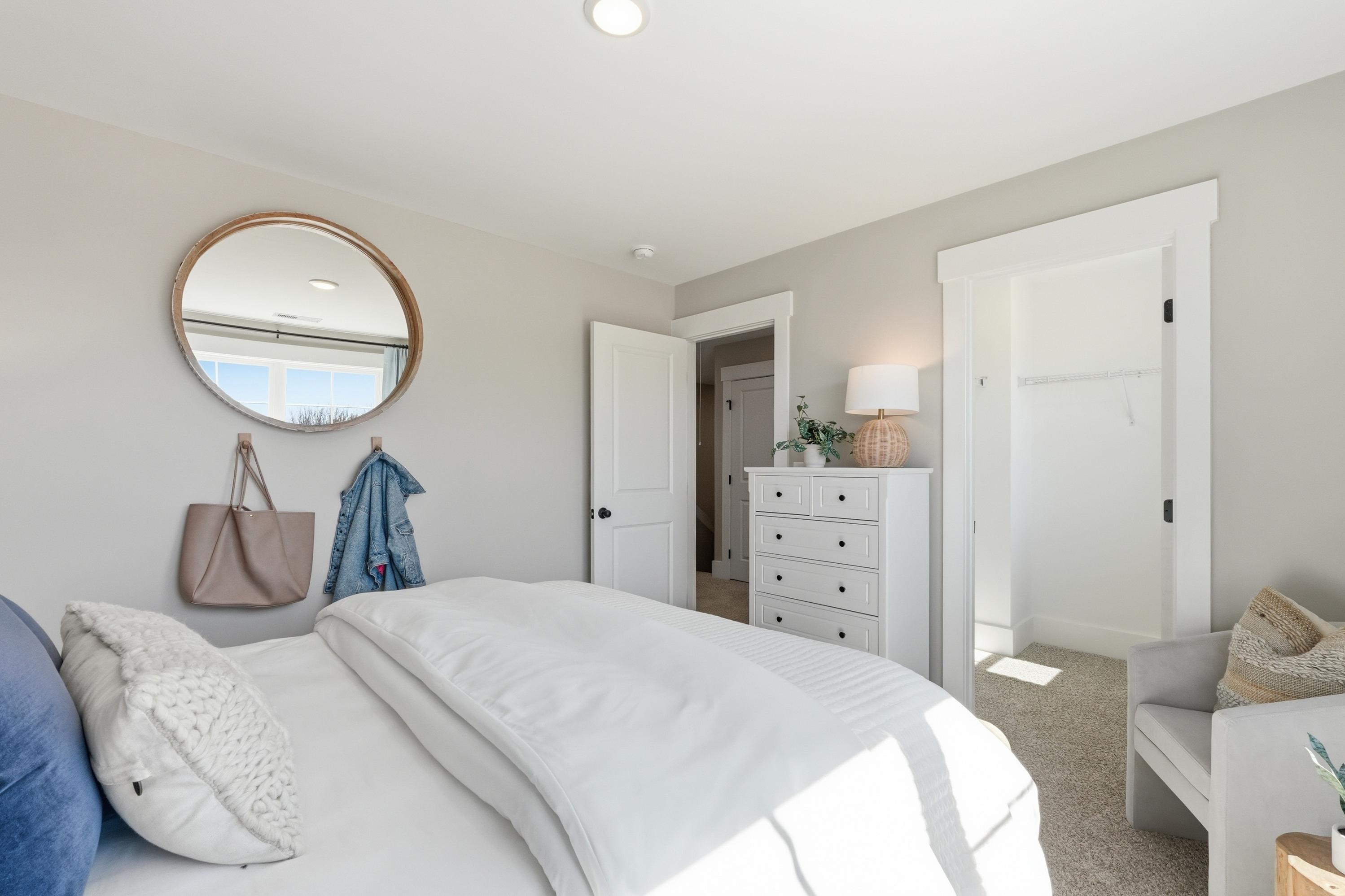 Cozy bedroom interior at Berry Cove in New Market, Alabama with white bed, round gold mirror, hanging purse, and dresser