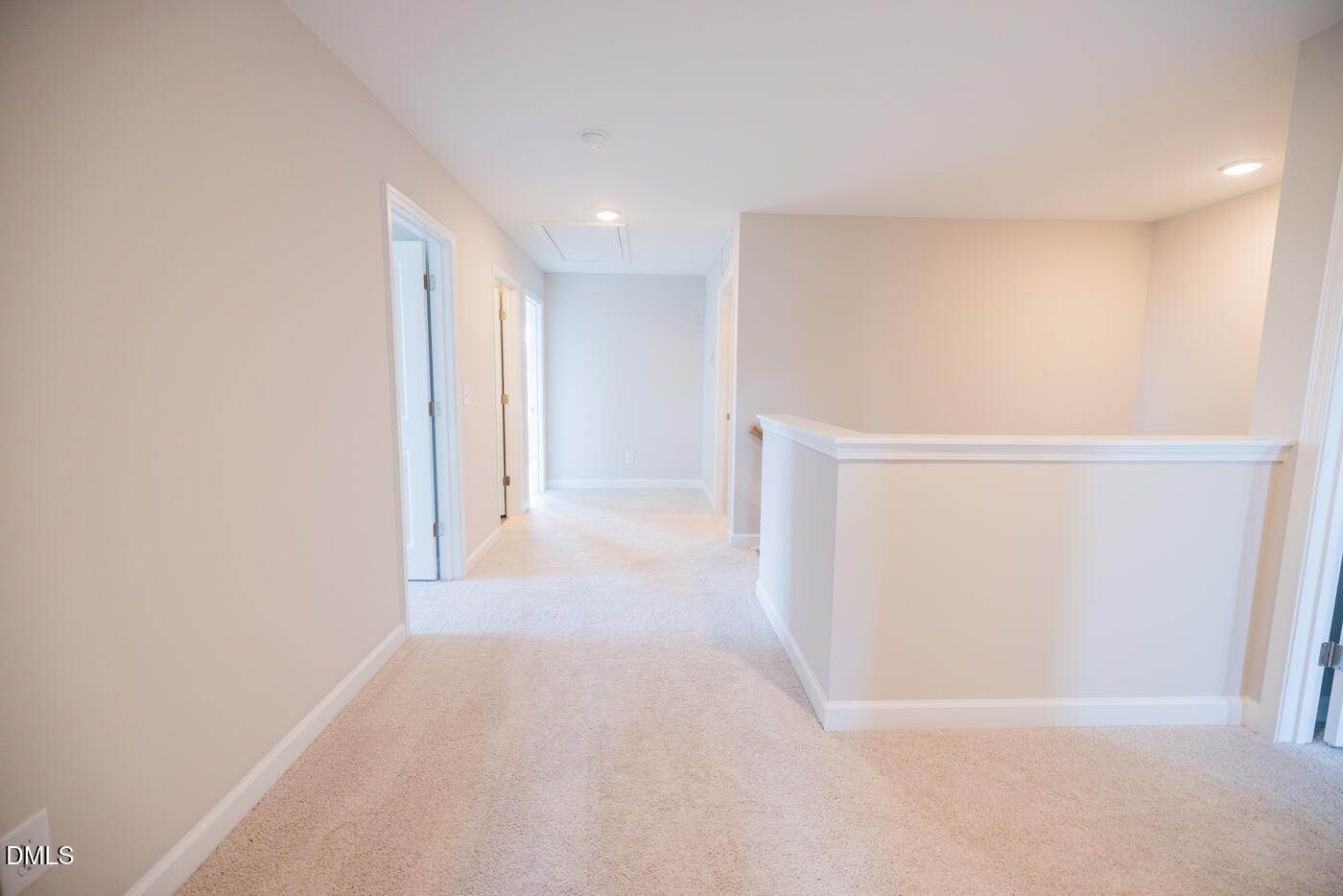 Bright upstairs hallway with beige carpet, neutral walls, open doors, and railing overlook in The Hickory II C, Zebulon, NC